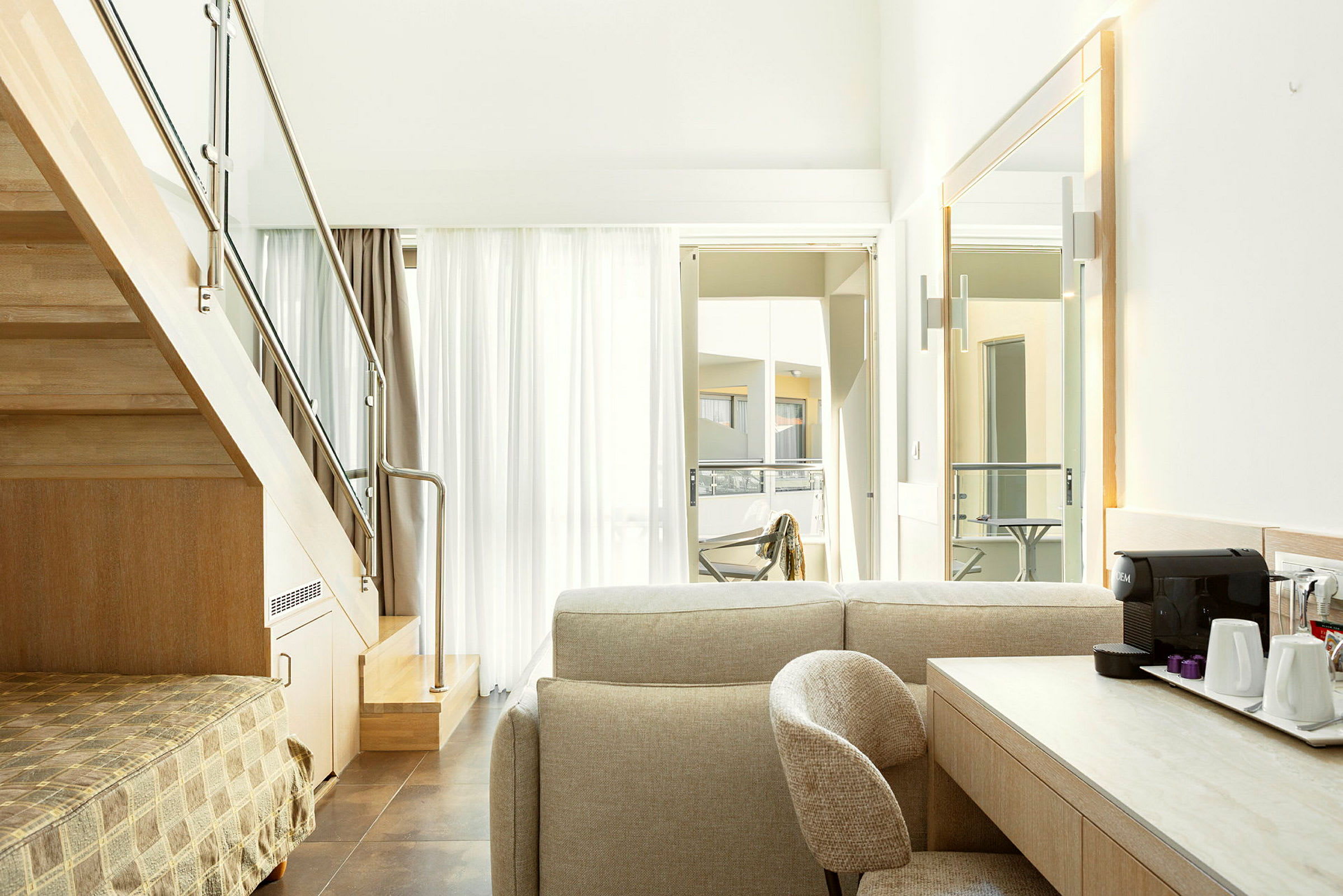 Interiørbilde av et moderne hotellrom med en trapp, sittegruppe og et skrivebord med kaffemaskin. (AI-generert tekst)