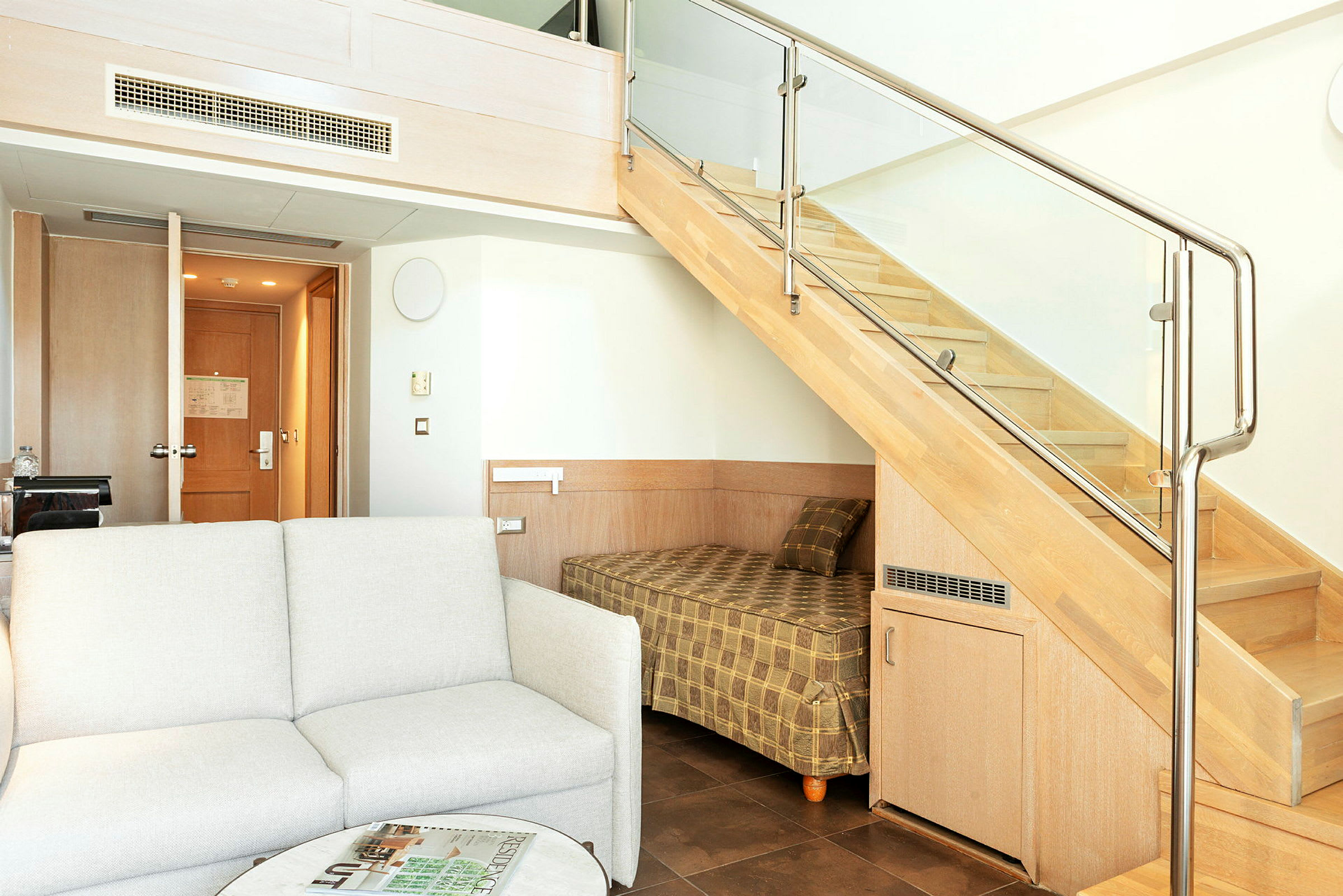 Et hotellrom med en sofa, et bord og en køyeseng under en trapp. (AI-generert tekst)