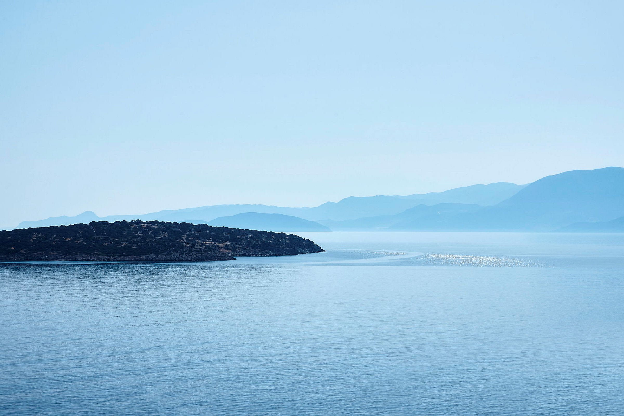 En utsikt over havet med en øy i forgrunnen og fjell i bakgrunnen. (AI-generert tekst)
