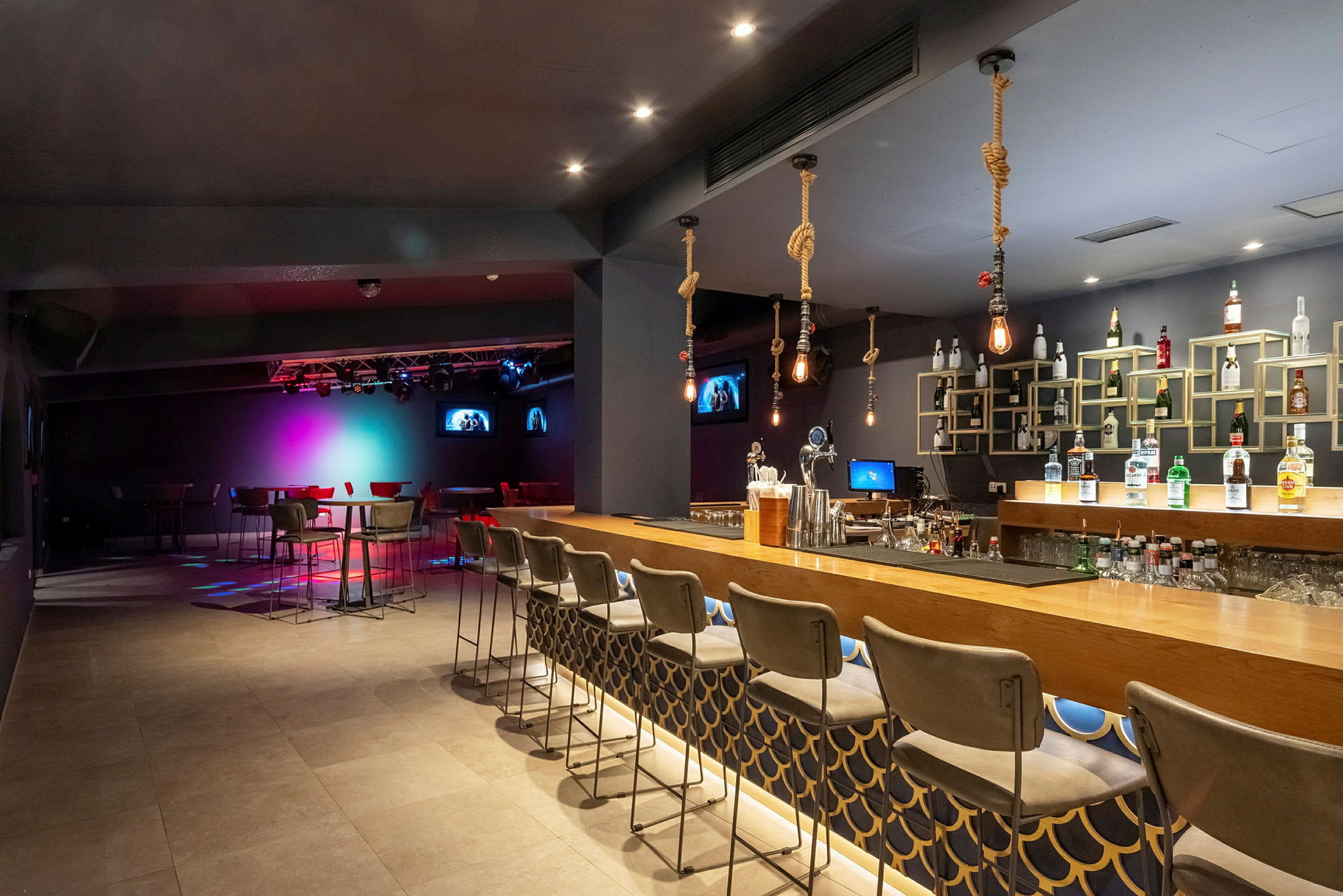 Innendørsbilde av en bar med sitteplasser og en opplyst scene i bakgrunnen. (AI-generert tekst)