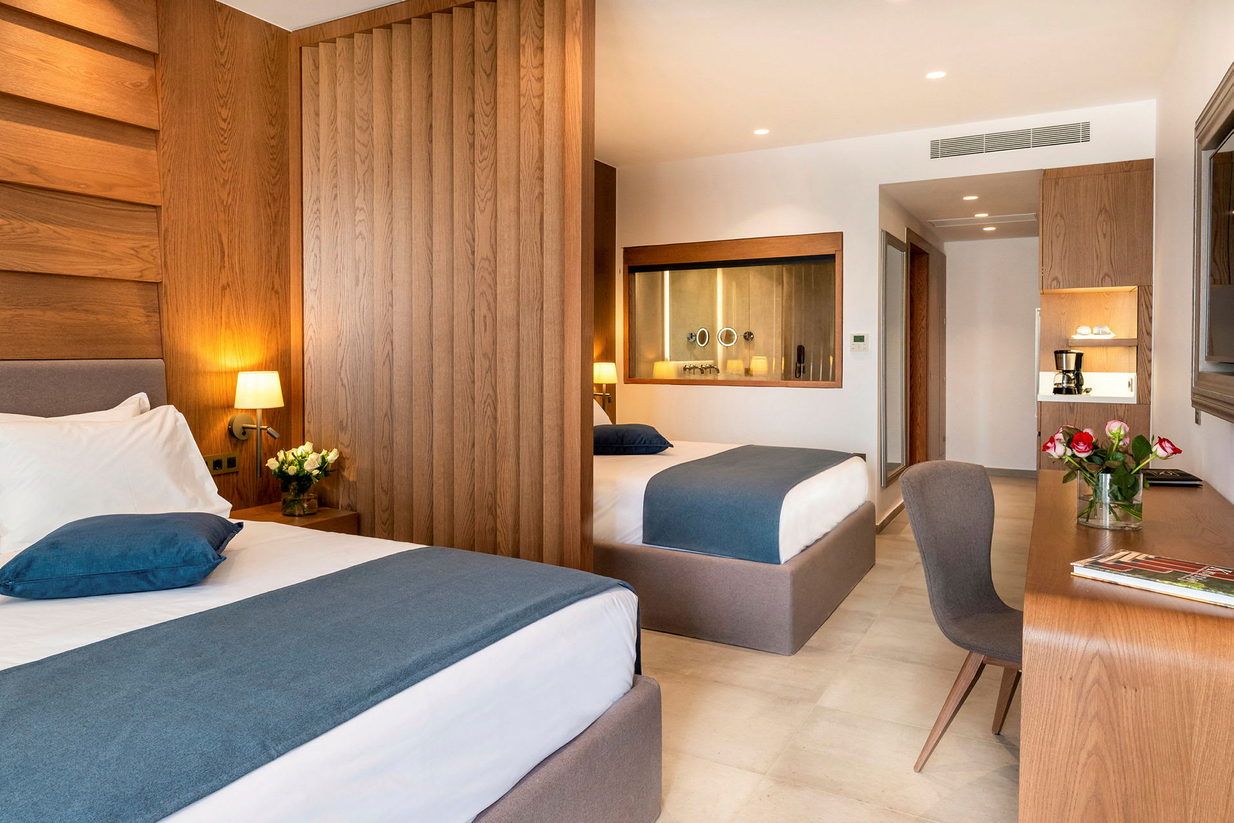 Et hotellrom med to senger, skrivebord og blomster. (AI-generert tekst)