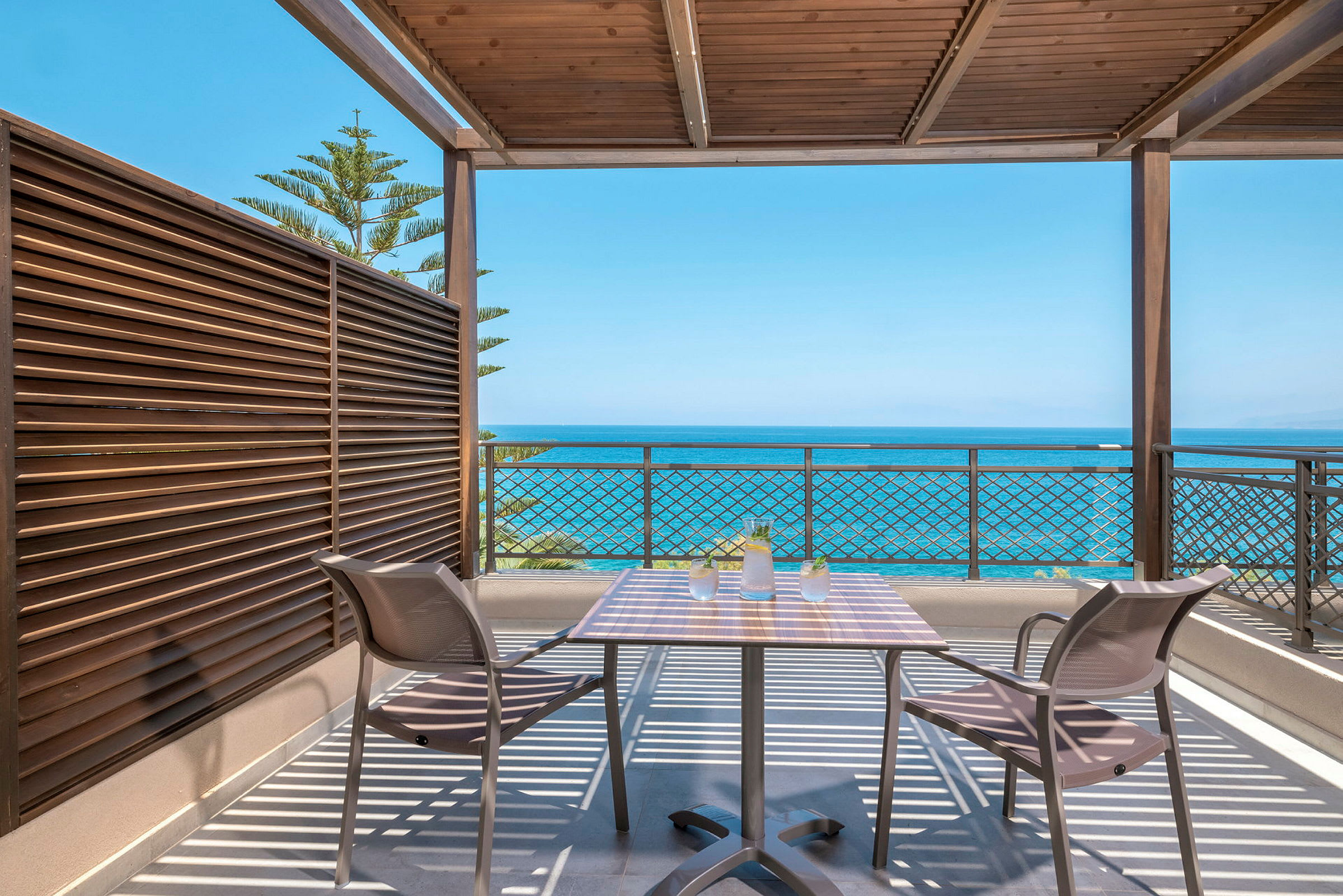 Terrasse med bord og stoler under tak med utsikt mot havet. (AI-generert tekst)