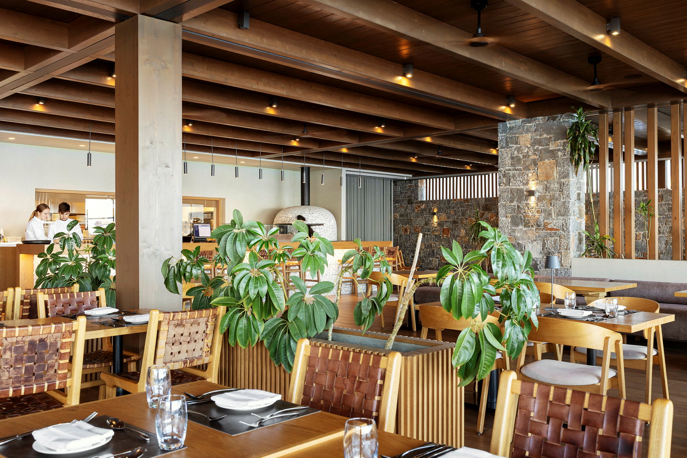Et moderne restaurantinteriør med tremøbler, grønne planter og steinvegger. (AI-generert tekst)