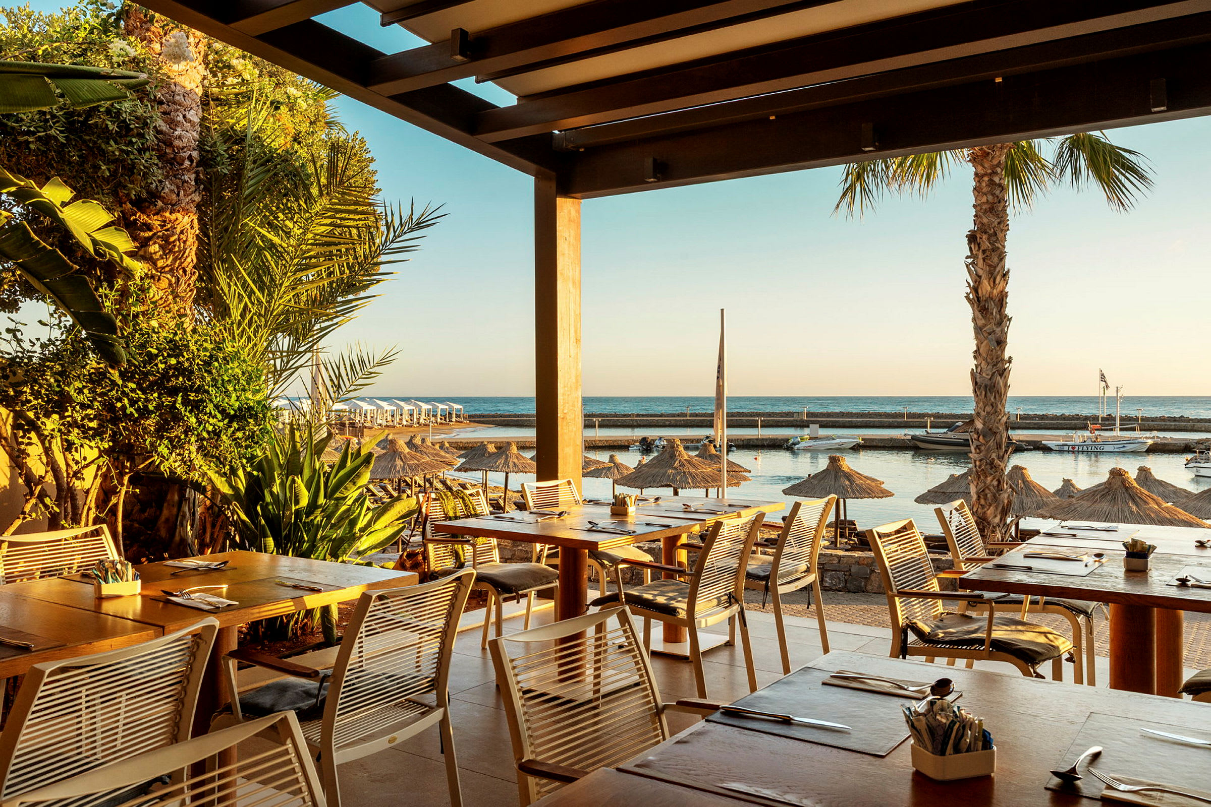 Utsikt fra en restaurant med havet i bakgrunnen og parasoller på stranden. (AI-generert tekst)