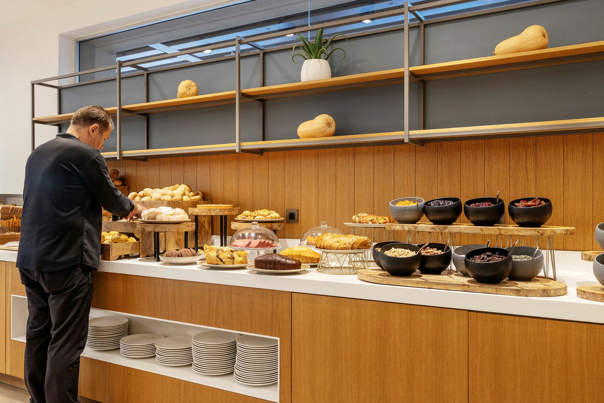 En person ved en buffé fylt med bakverk som brød og muffins, samt boller med forskjellige ingredienser. (AI-generert tekst)