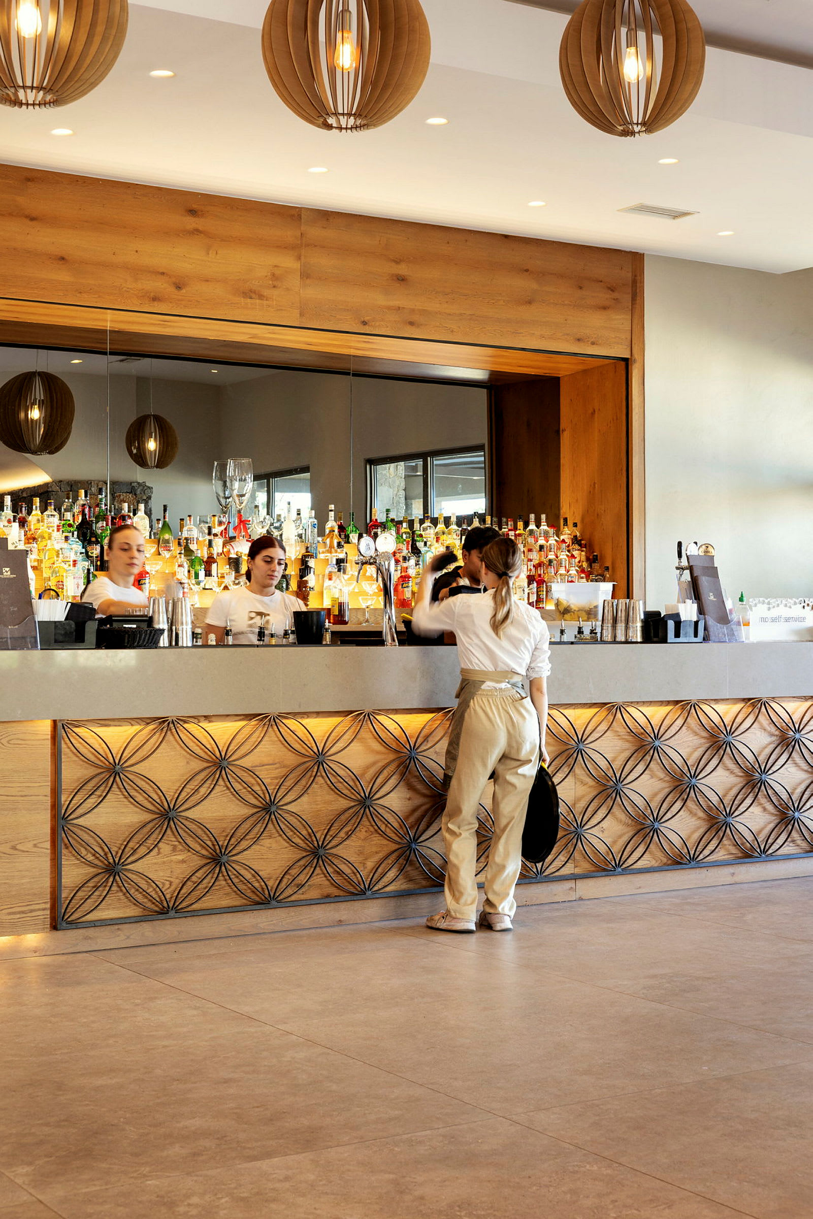 En bartender og kunder ved en elegant bar med flasker og glass i bakgrunnen. (AI-generert tekst)
