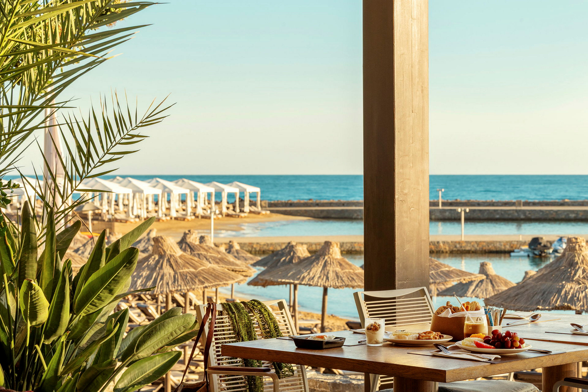 Bilde av en strandrestaurant med utsikt over havet, parasoller og bord dekket med måltider. (AI-generert tekst)