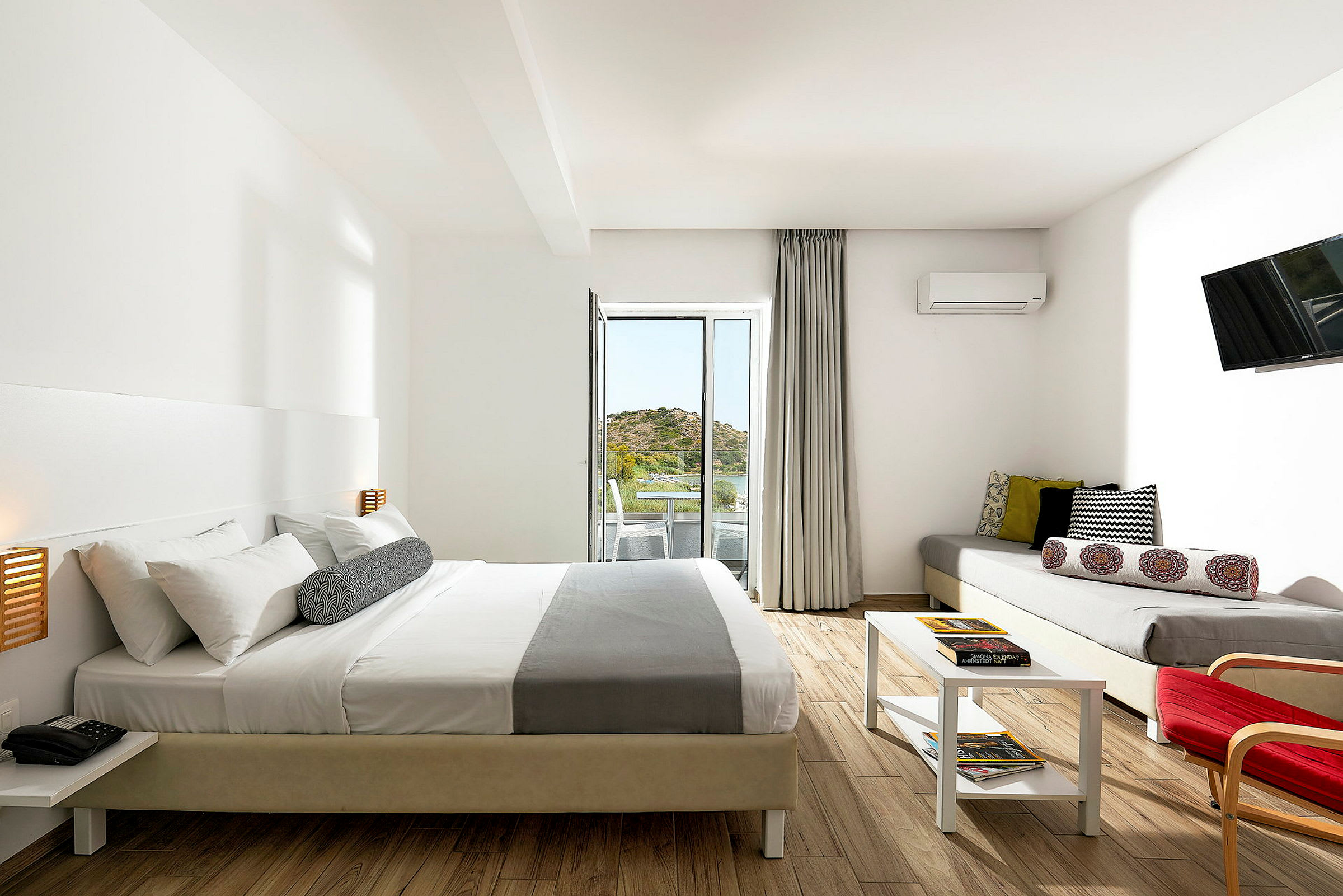 Et moderne hotellrom med dobbeltseng, sofa, bord og balkong med utsikt. (AI-generert tekst)