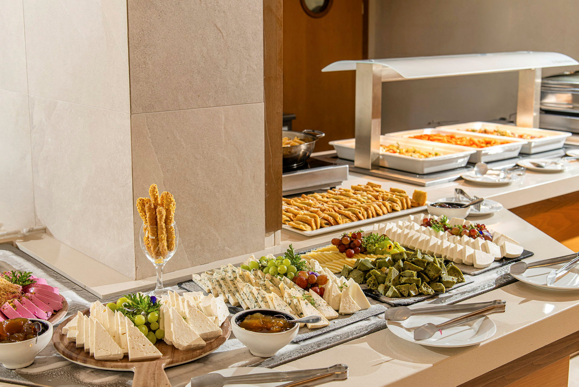 En buffet med et utvalg av ost, kjeks, frukt og varme retter på tallerkener. (AI-generert tekst)