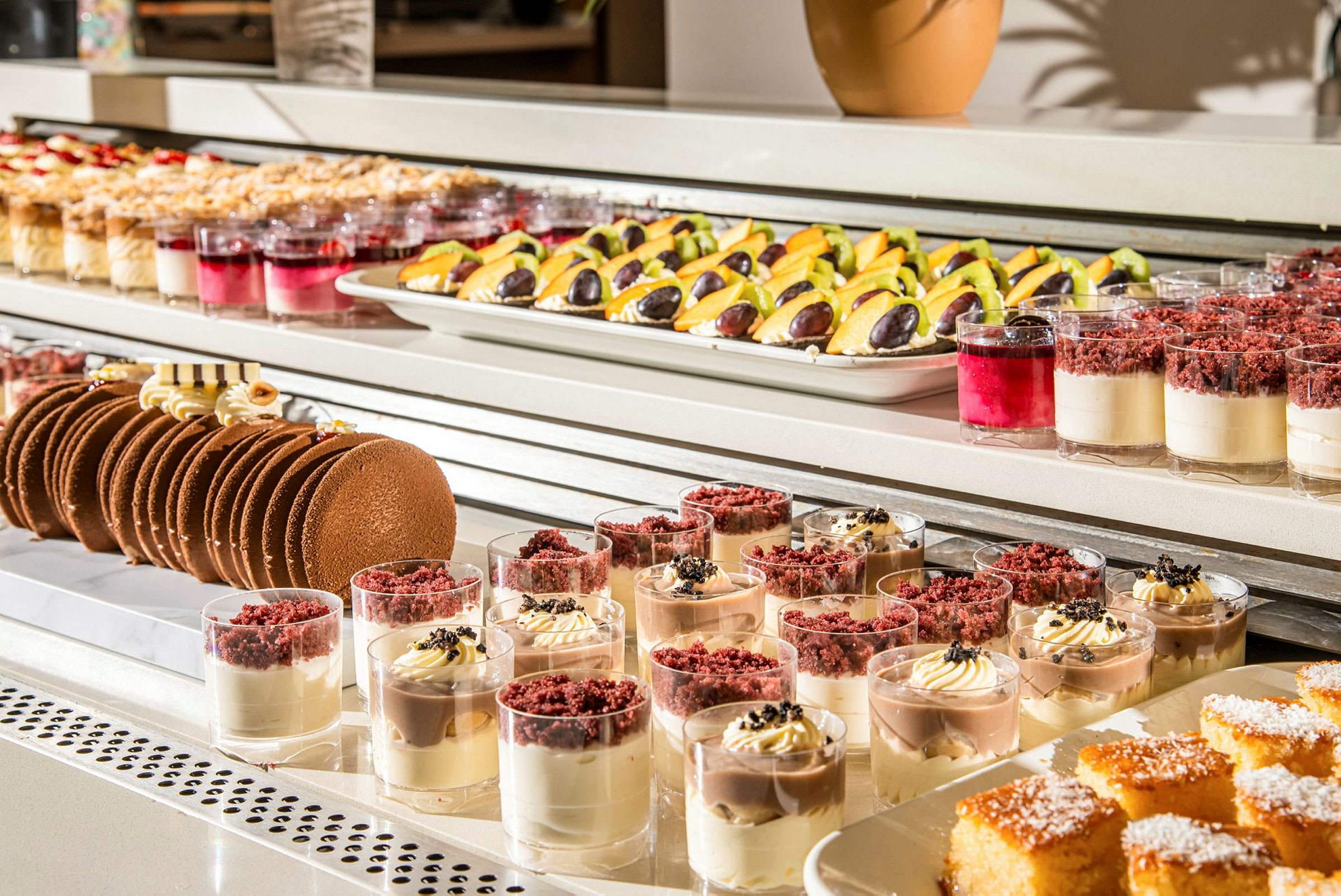 Bildet viser en buffé med forskjellige desserter, inkludert små desserter i glass, kaker og fruktpynt. (AI-generert tekst)