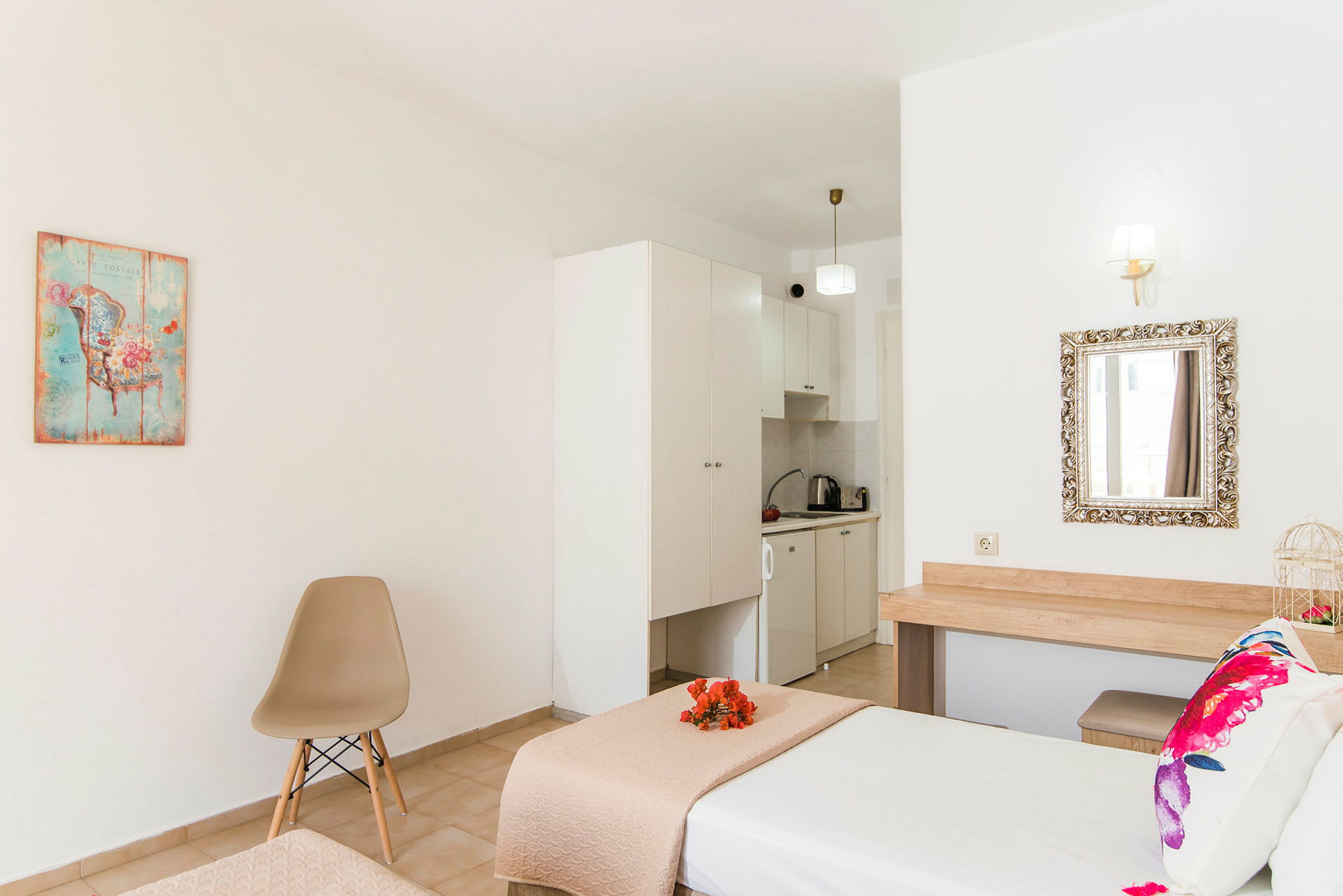 Et hotellrom med seng, stol, dekorativt bilde og et lite kjøkkenområde. (AI-generert tekst)