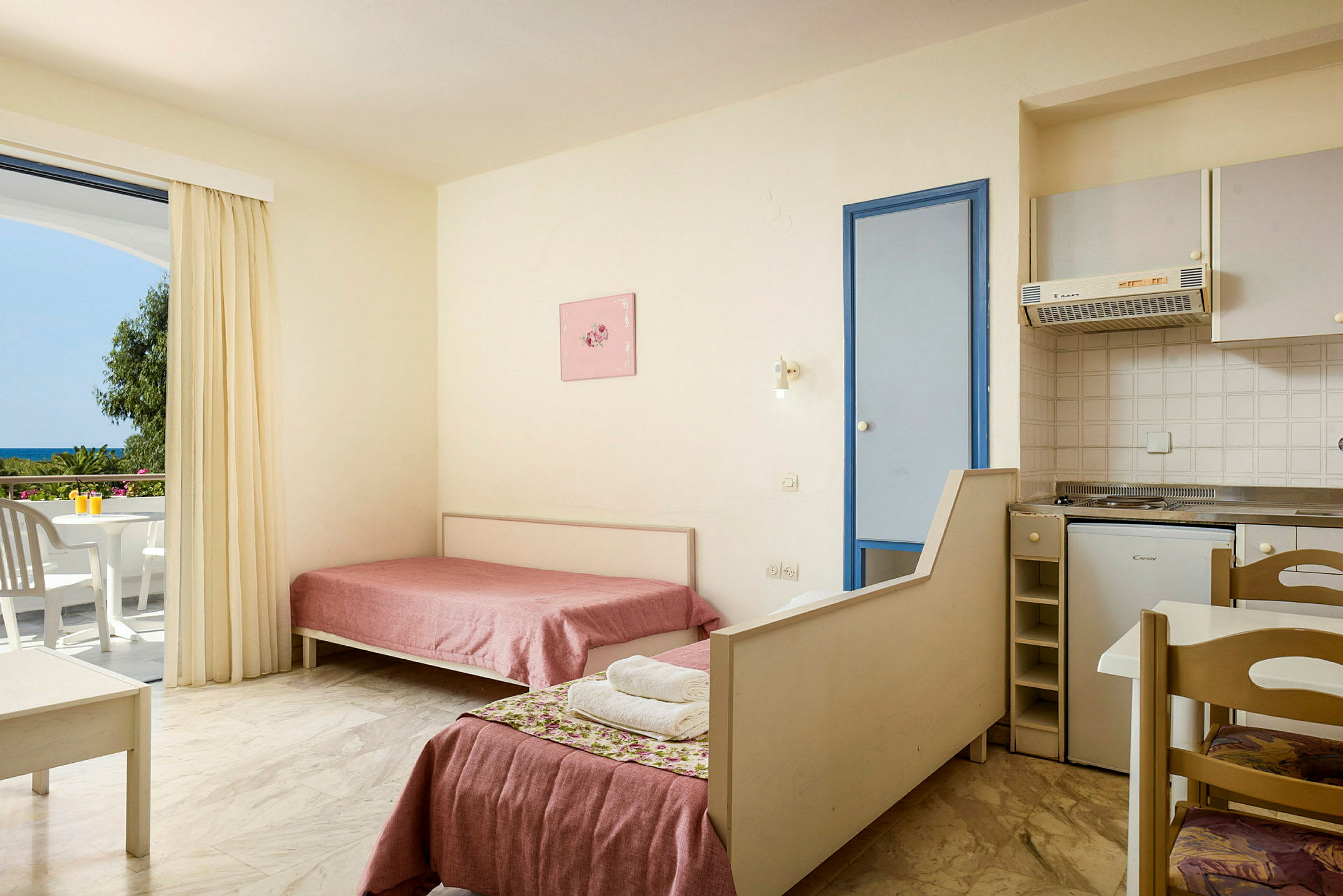 Interiør av et hotellrom med to enkeltsenger, et lite kjøkken og en balkong med utsikt. (AI-generert tekst)