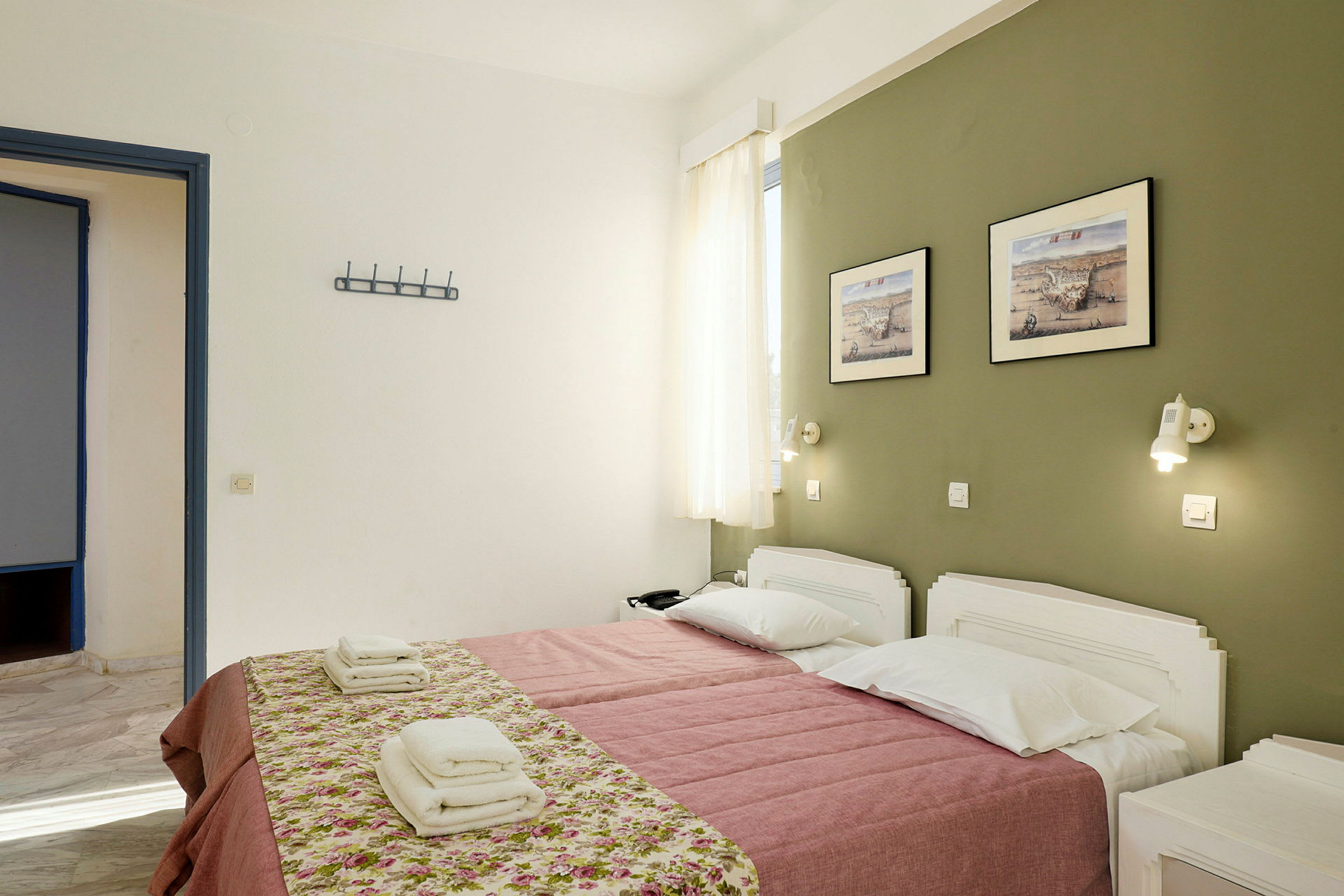 Et hotellrom med to enkeltsenger oppredd med rosa sengeteppe og blomstrete overkast. På veggen henger to bilder over sengene. (AI-generert tekst)
