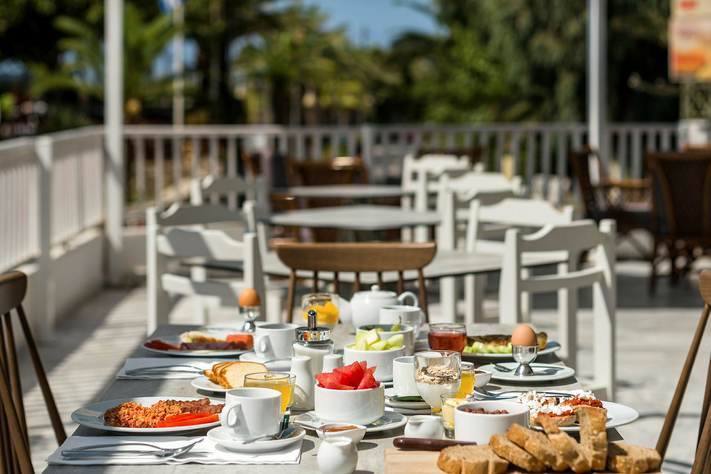 Et bord fylt med frokostmat, med flere bord og stoler i bakgrunnen. (AI-generert tekst)