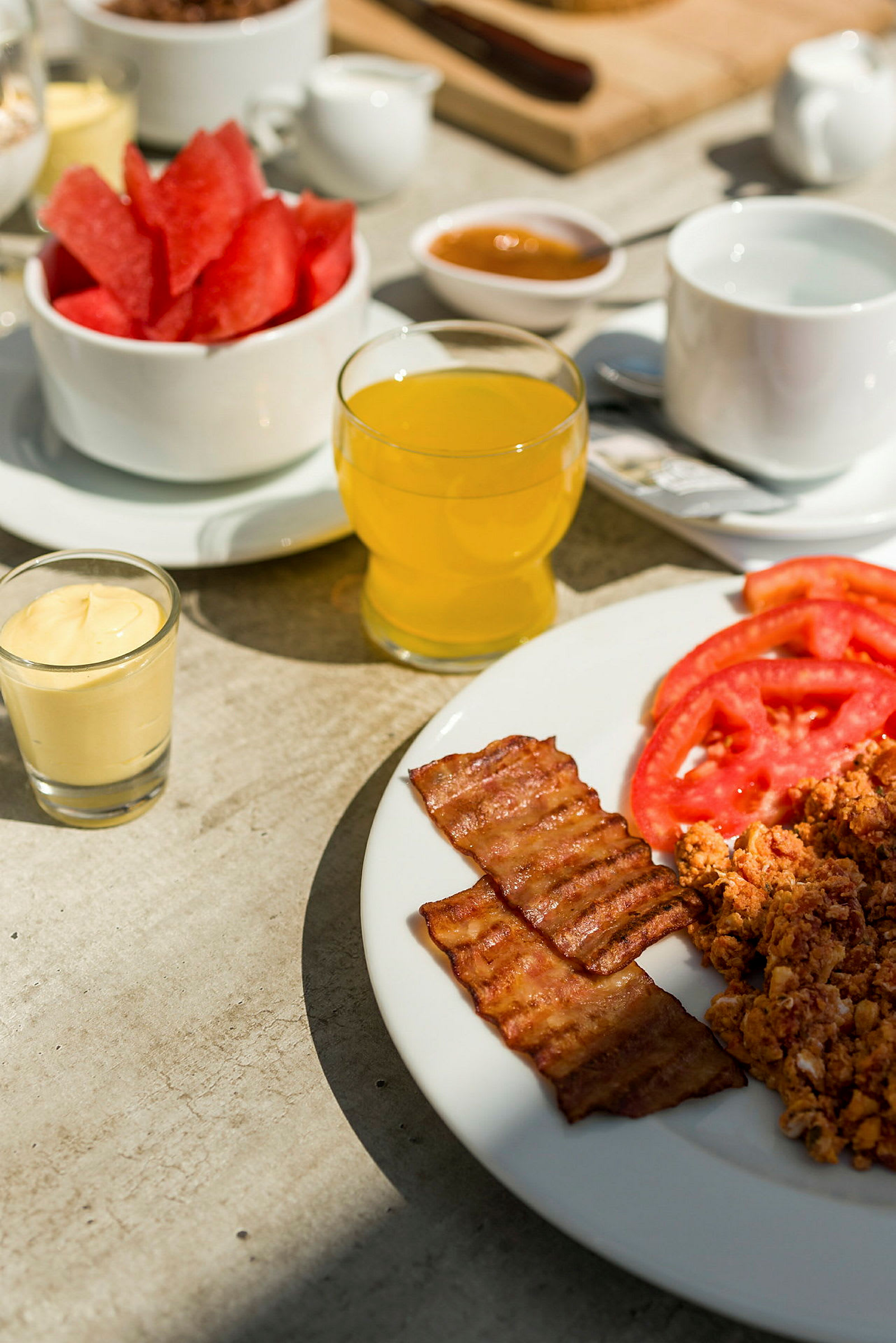 En frokost med bacon, skivede tomater, eggerøre og forskjellige drikkevarer. (AI-generert tekst)