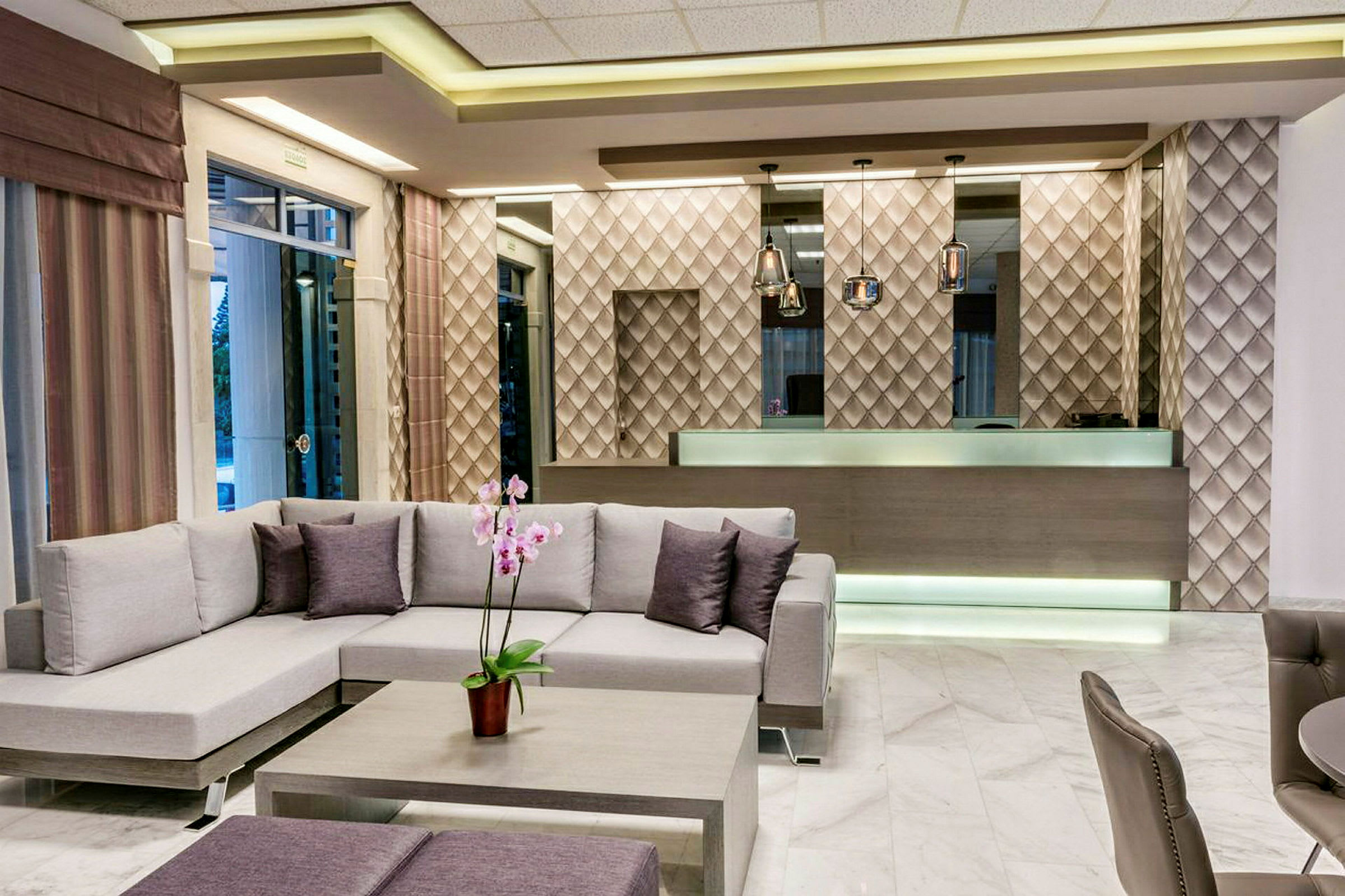 Hotellobbyen med moderne innredning, inkludert en sofa og et resepsjonsområde med designt vegg og lamper. (AI-generert tekst)