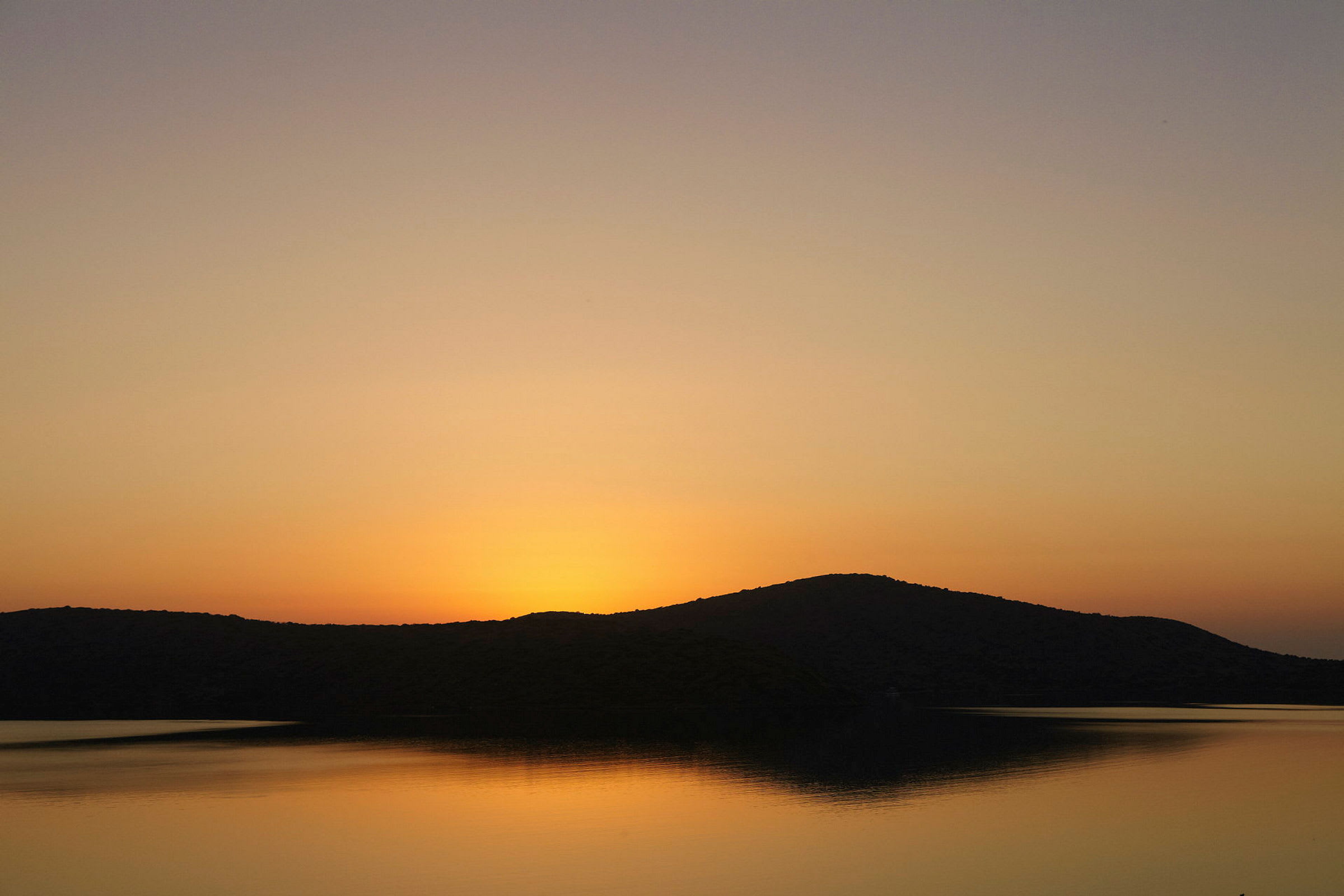 Solnedgang over en innsjø med silhuetter av åser. (AI-generert tekst)