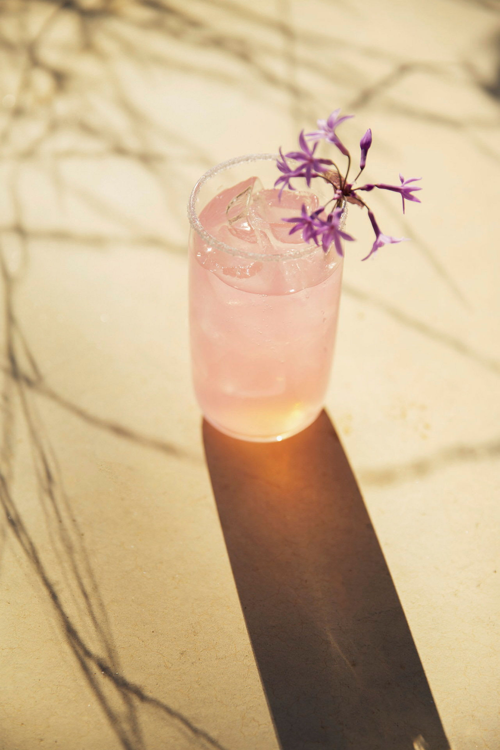 Et glass med en rosa drikk og is, dekorert med lilla blomster. (AI-generert tekst)