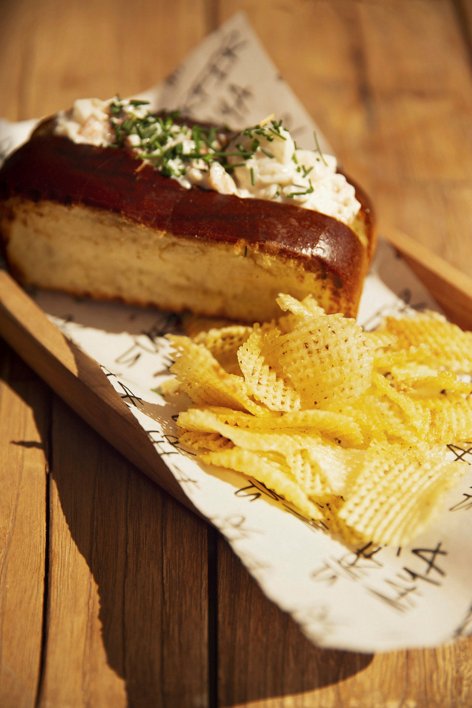 Brød med pålegg og chips på et trebord. (AI-generert tekst)