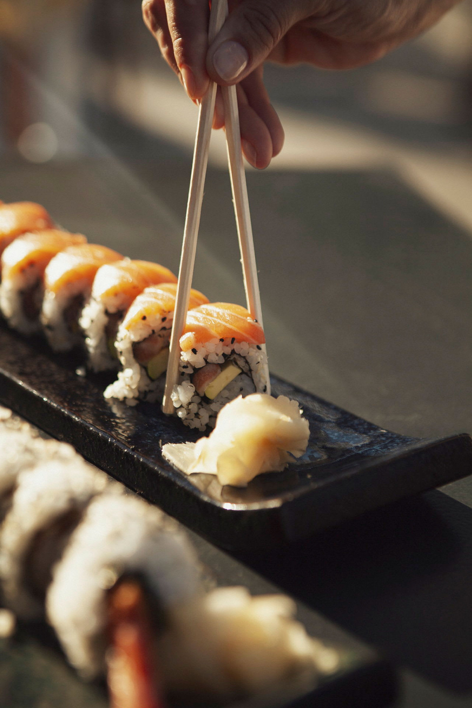 Hånd holder spisepinner og tar sushi fra et fat. (AI-generert tekst)