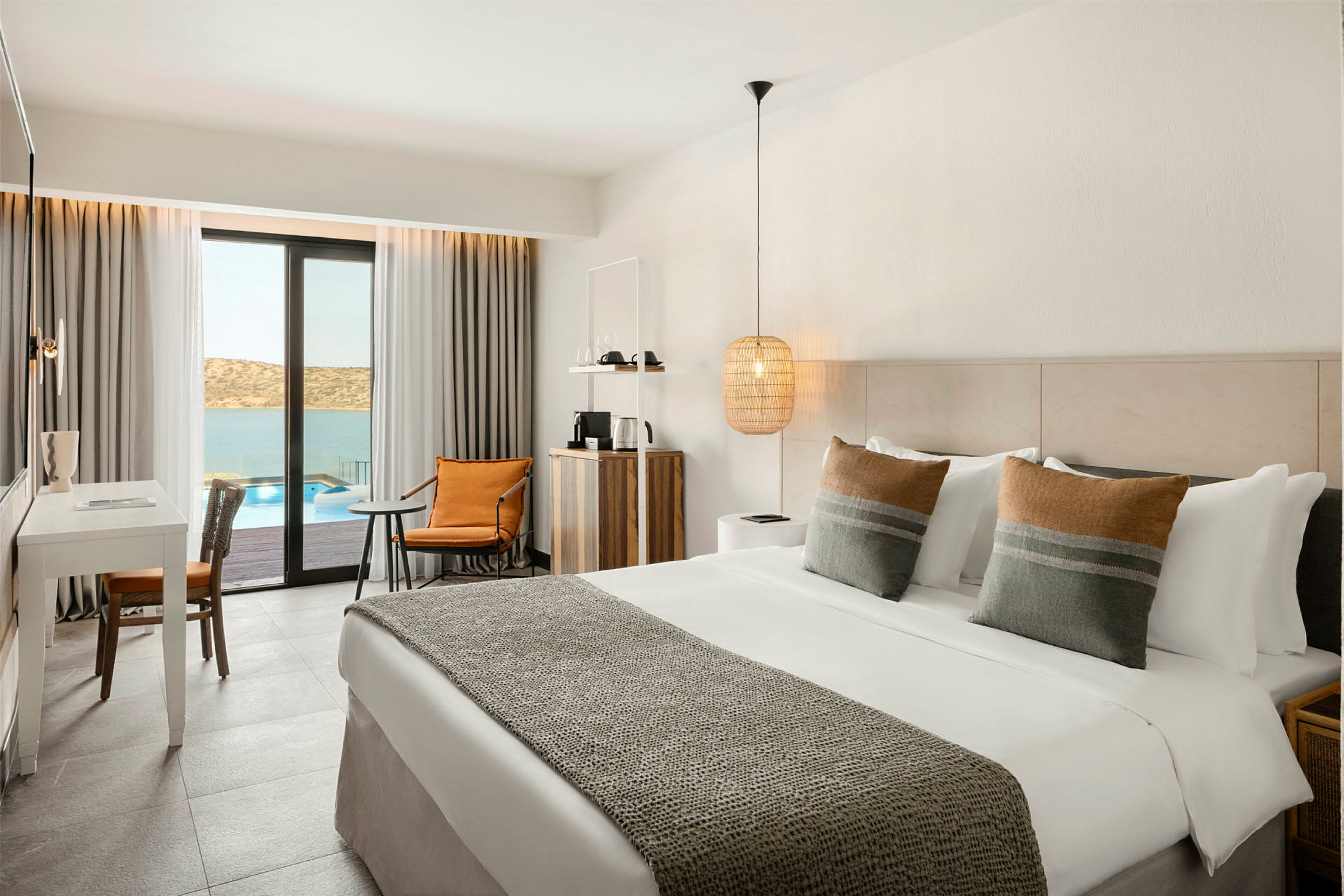 Hotellrom med dobbeltseng, skrivebord og sittegruppe, med utsikt over basseng og sjø. (AI-generert tekst)