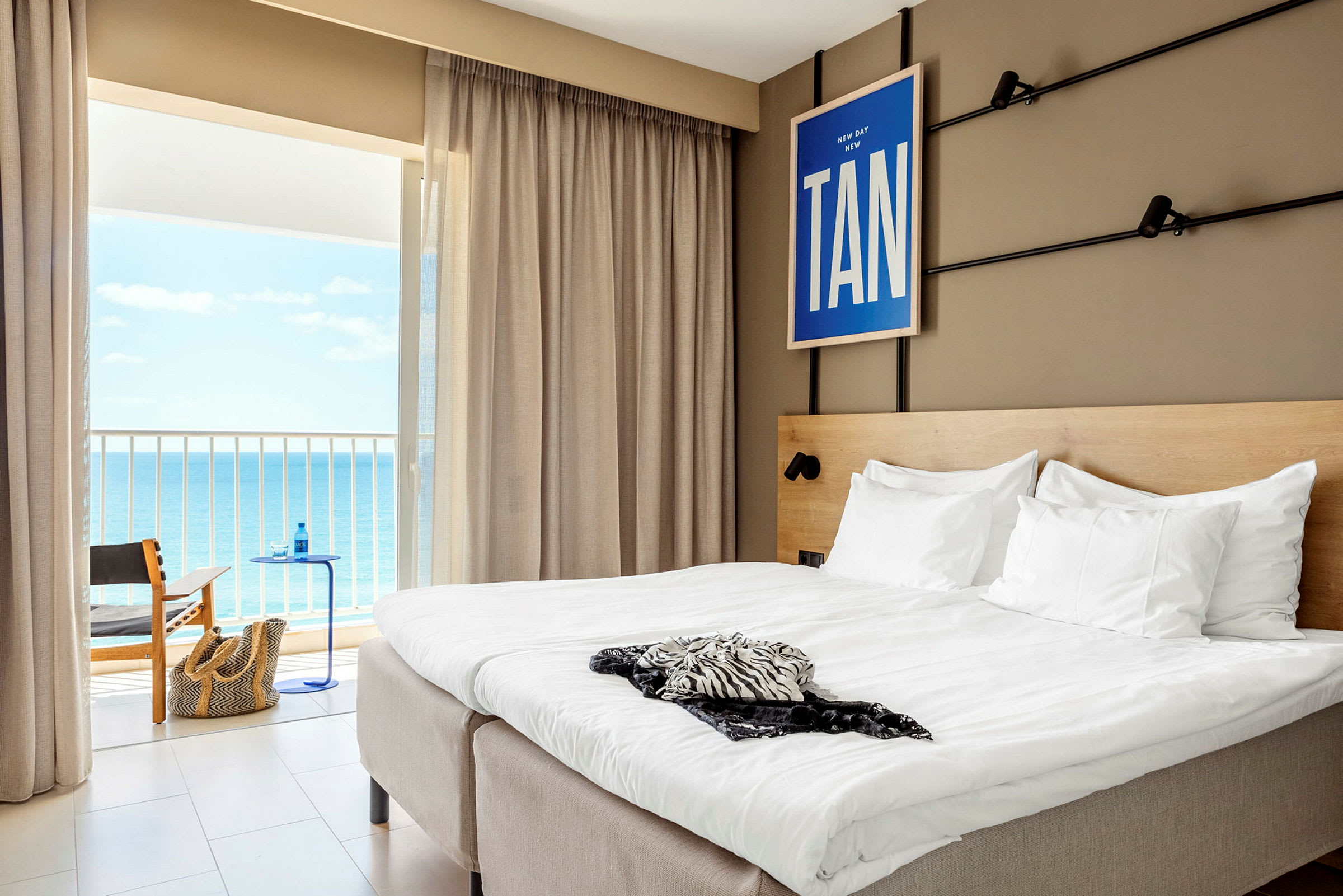 Hotellrom med en dobbeltseng og utsikt mot havet gjennom balkongdøren. (AI-generert tekst)