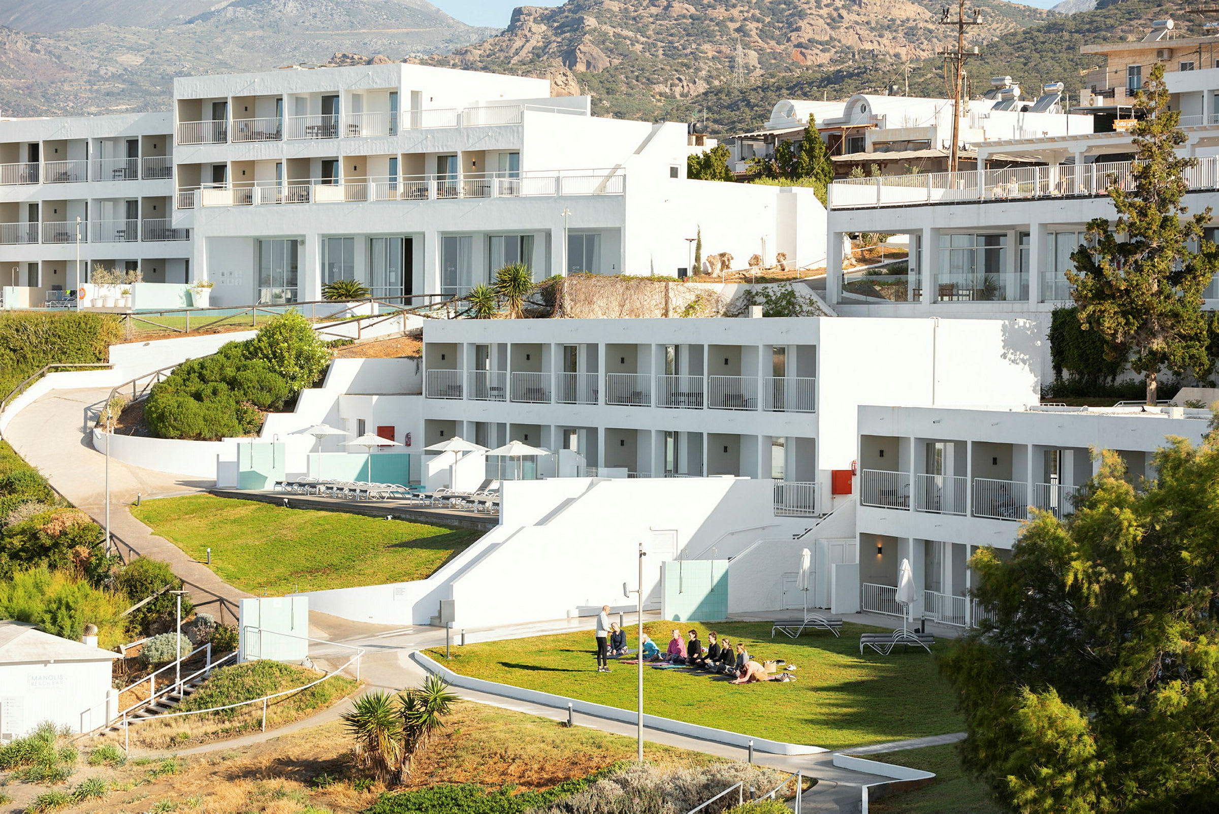 Moderne hotellbygg med hvite fasader og balkonger, med personer som sitter på grønt gress i forgrunnen. (AI-generert tekst)