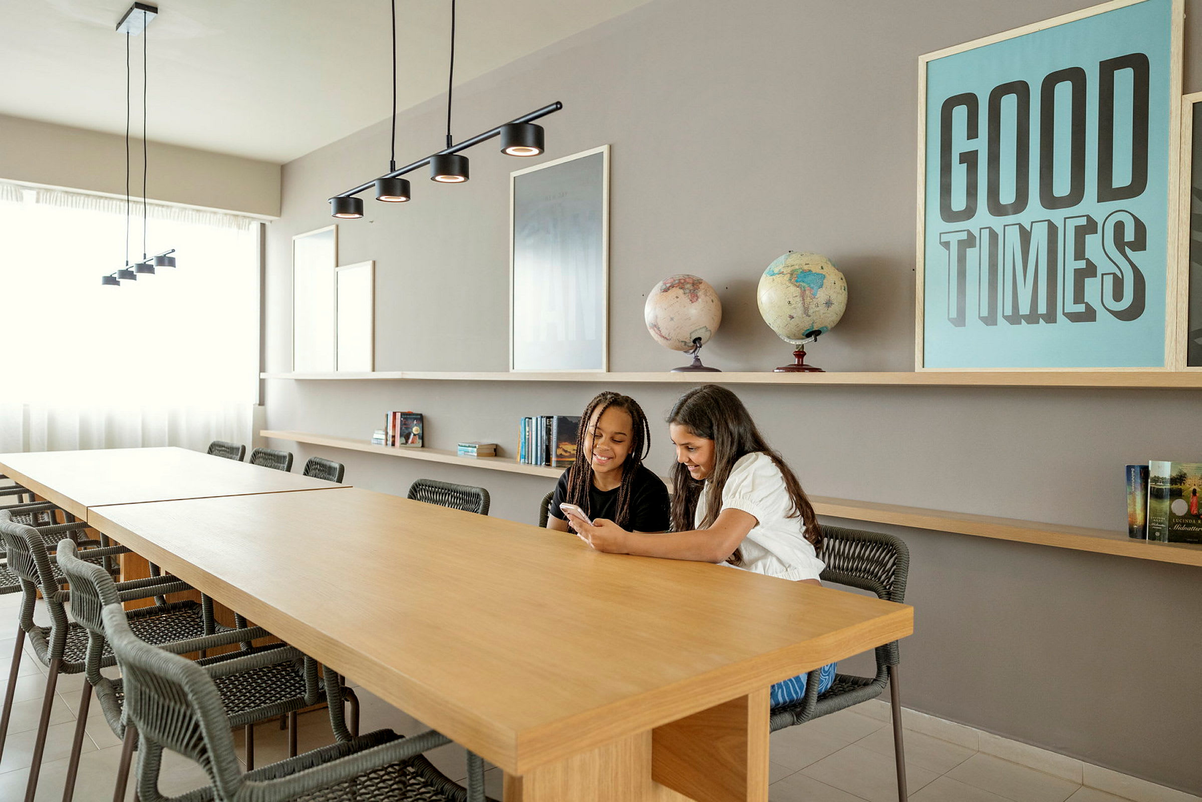 Et moderne innredet rom med et langbord, hyller, bøker, globuser og en plakat med teksten 'GOOD TIMES'. (AI-generert tekst)