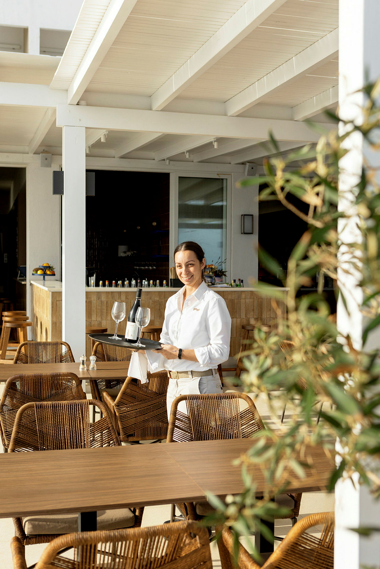 Servitør bærer et brett med vin og glass på en restaurantterrasse. (AI-generert tekst)