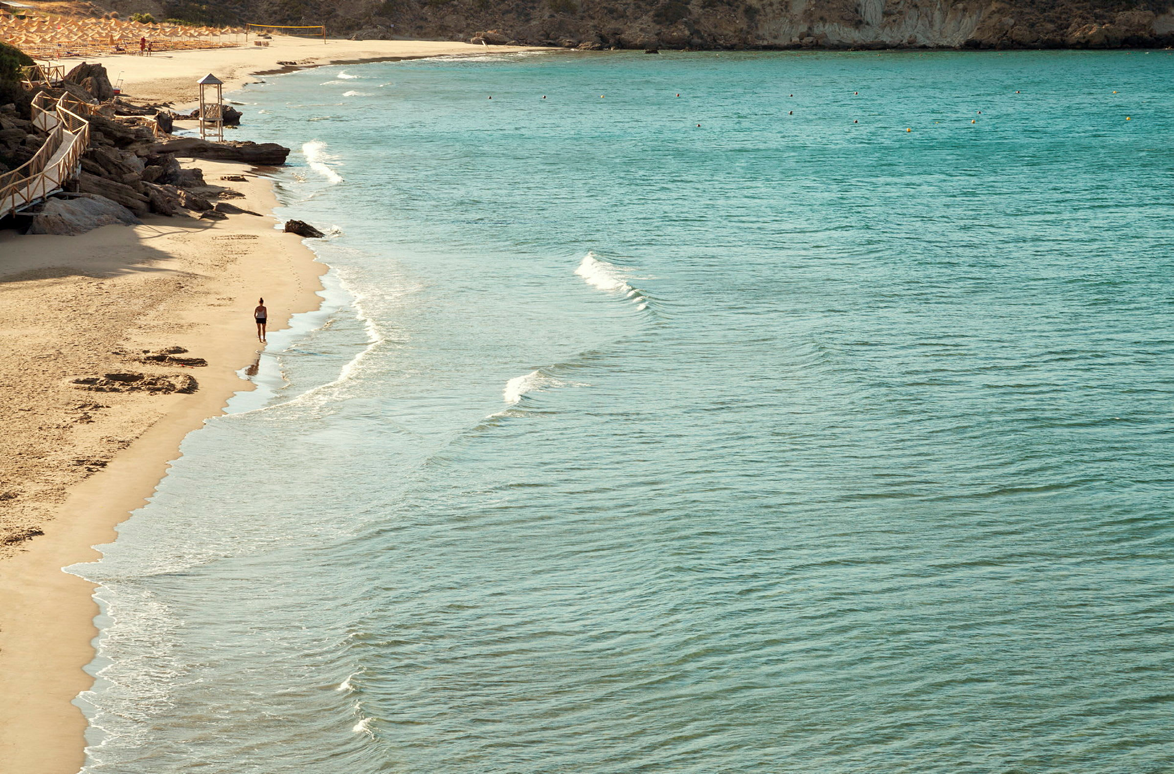 Strand med klart vann og en person som går langs vannkanten. (AI-generert tekst)