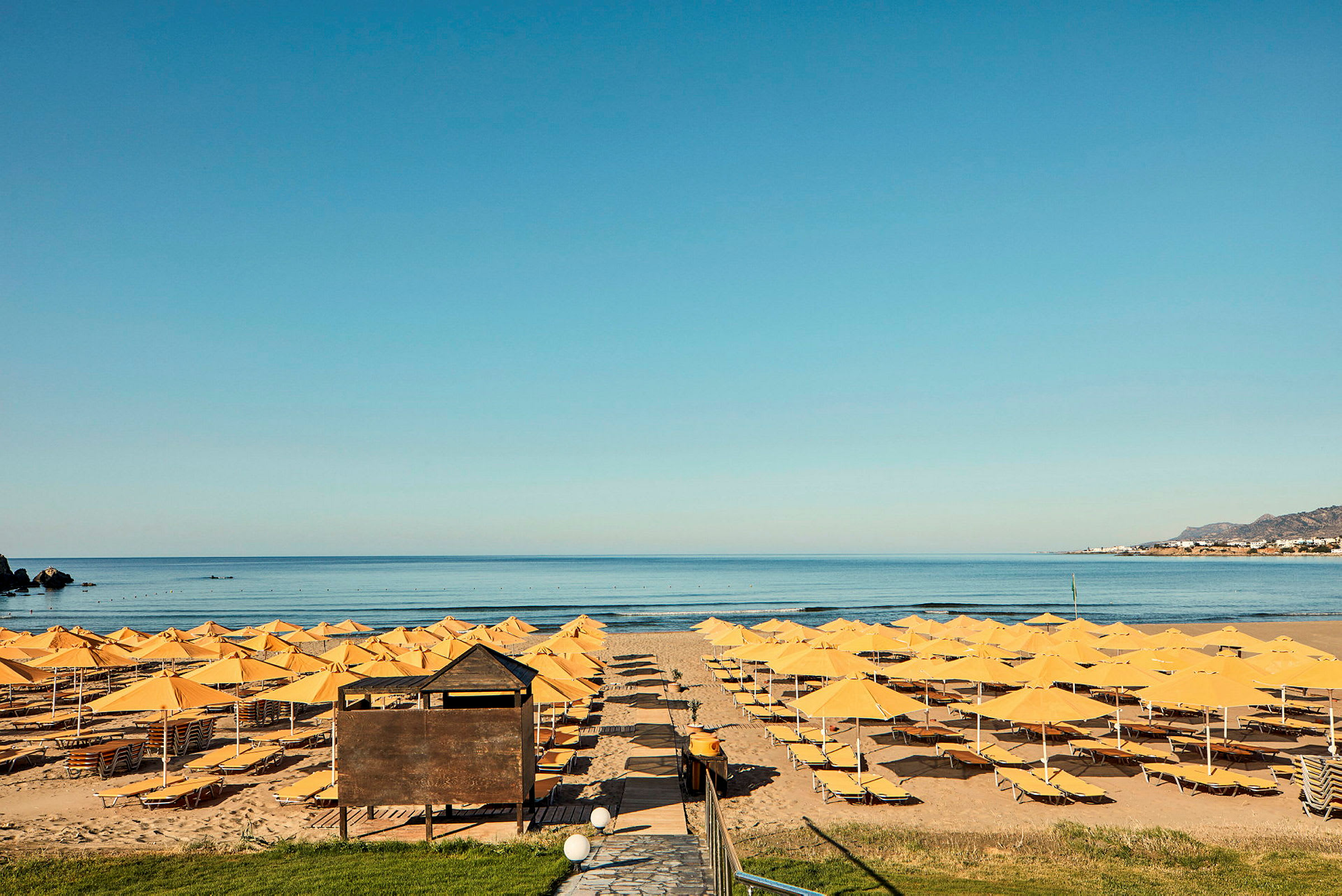 Strand med gule parasoller og solsenger foran havet. (AI-generert tekst)