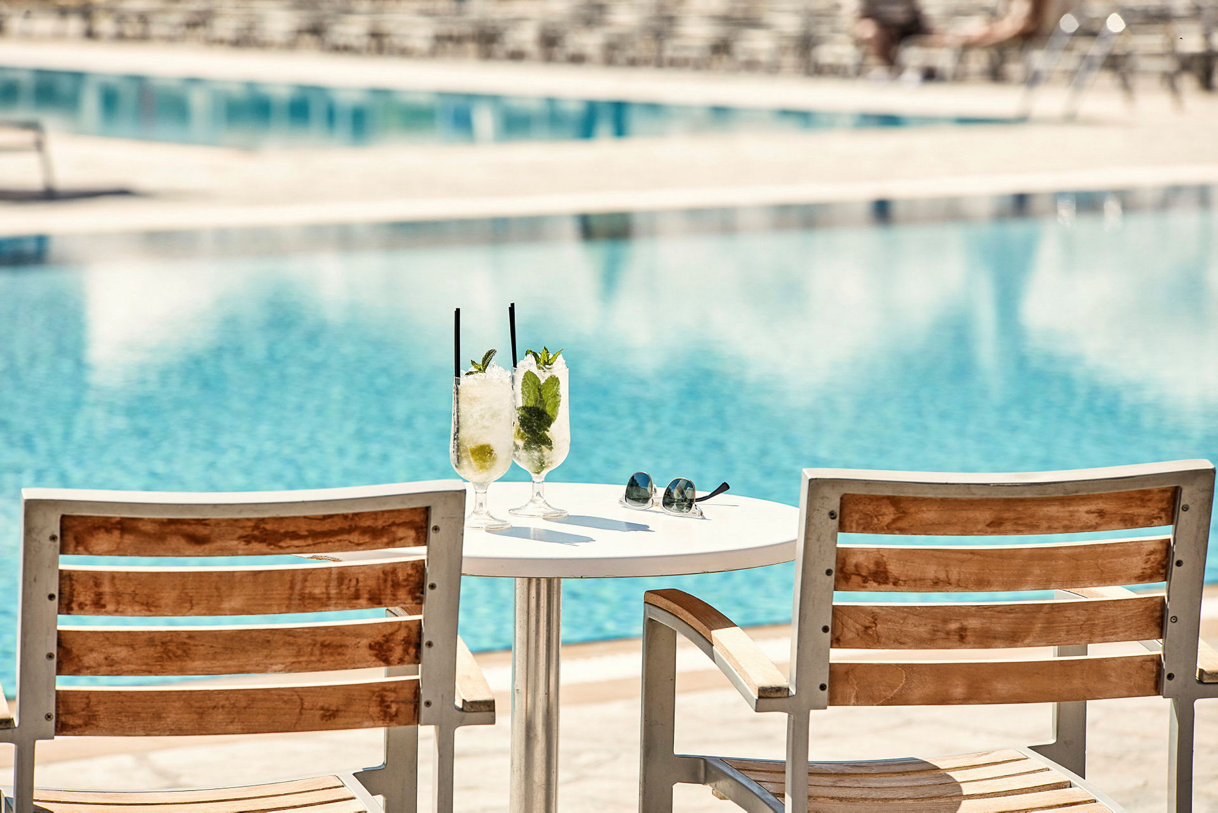 To solsenger og et bord med to glass med drinker ved et basseng. (AI-generert tekst)