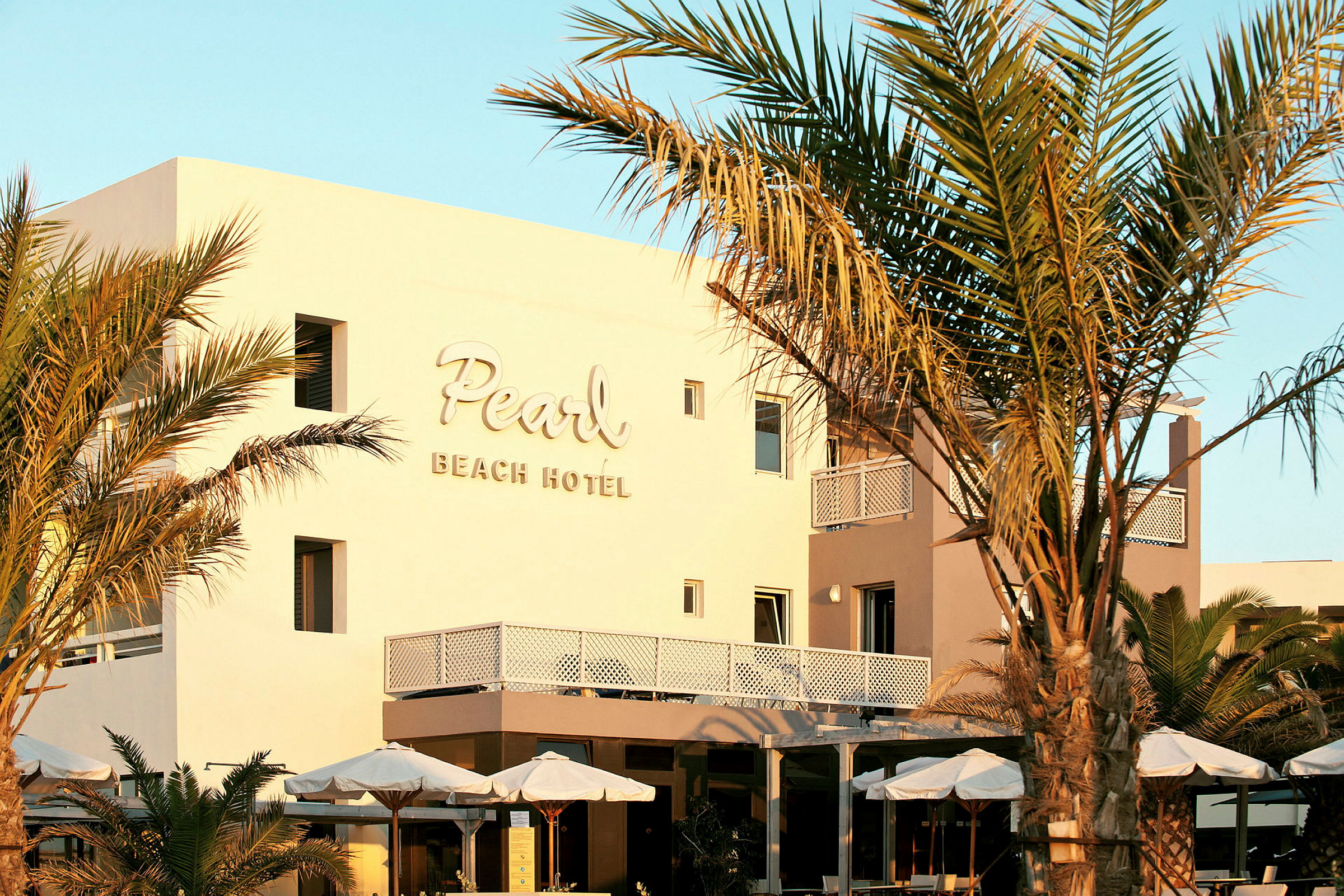 Fasaden til Pearl Beach Hotel med omkringliggende palmer og parasoller. (AI-generert tekst)