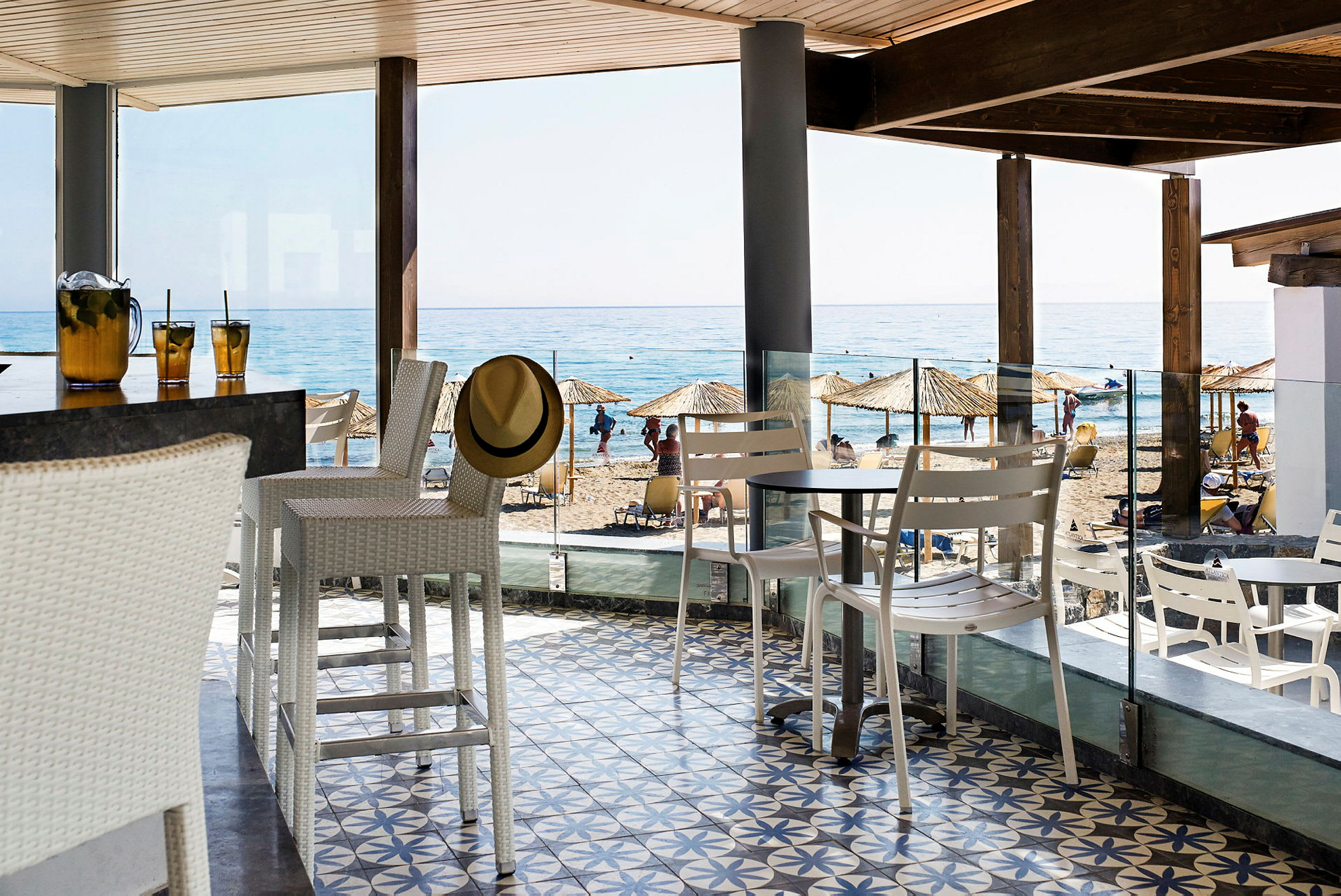 En strandbar med hvit innredning. I bakgrunnen er det en sandstrand og havet. (AI-generert tekst)