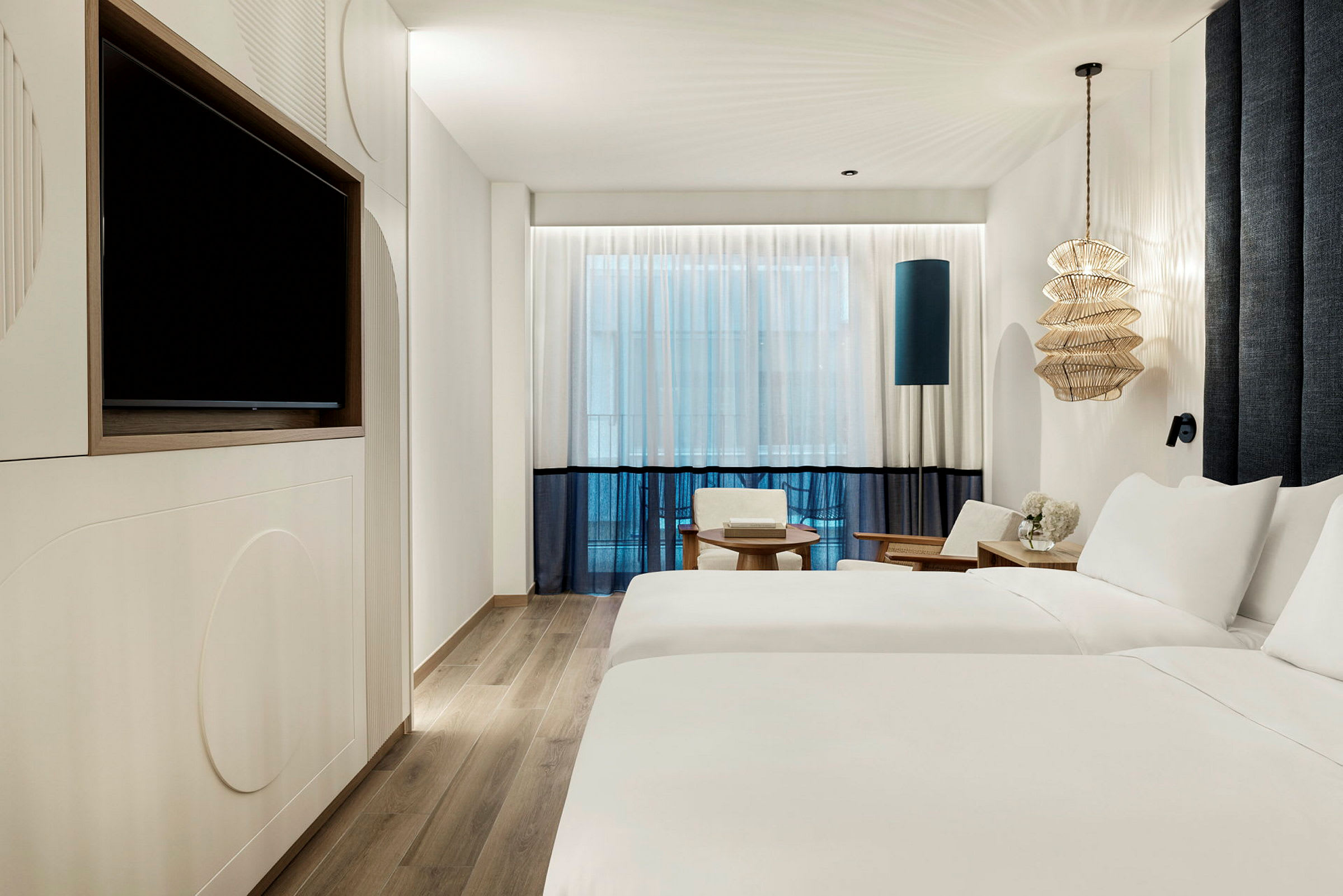 Et moderne hotellrom med to enkeltsenger, en TV på veggen, sittemøbler og en dekorativ lampe. (AI-generert tekst)