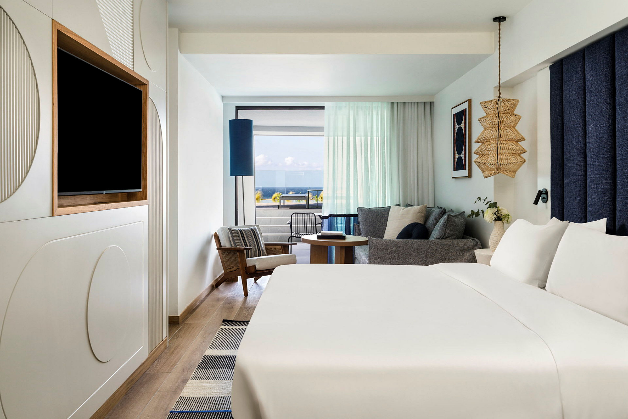 Et hotellrom med stor seng, en sittegruppe med glass mot balkong og havutsikt. (AI-generert tekst)