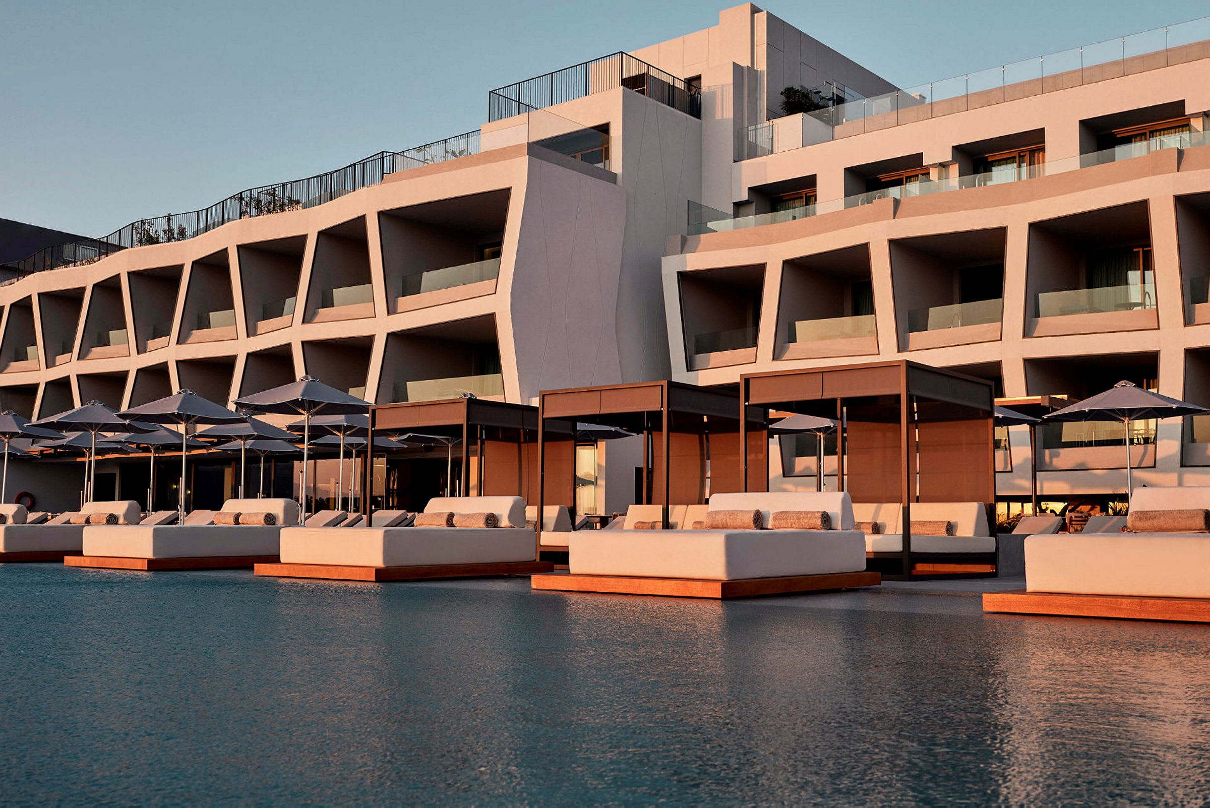 Moderne hotellbygning med solsenger og parasoller ved et basseng. (AI-generert tekst)