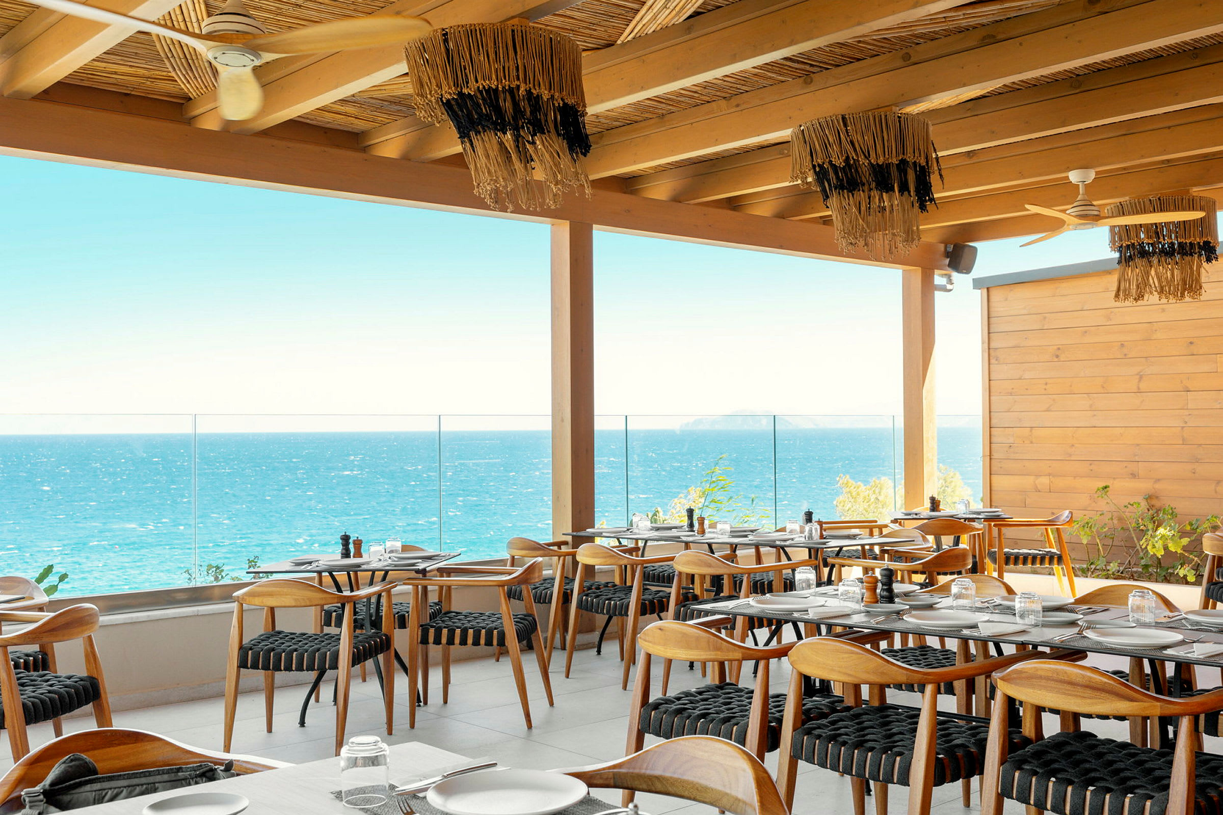Restaurant med tremøbler og havutsikt fra en terrasse. (AI-generert tekst)