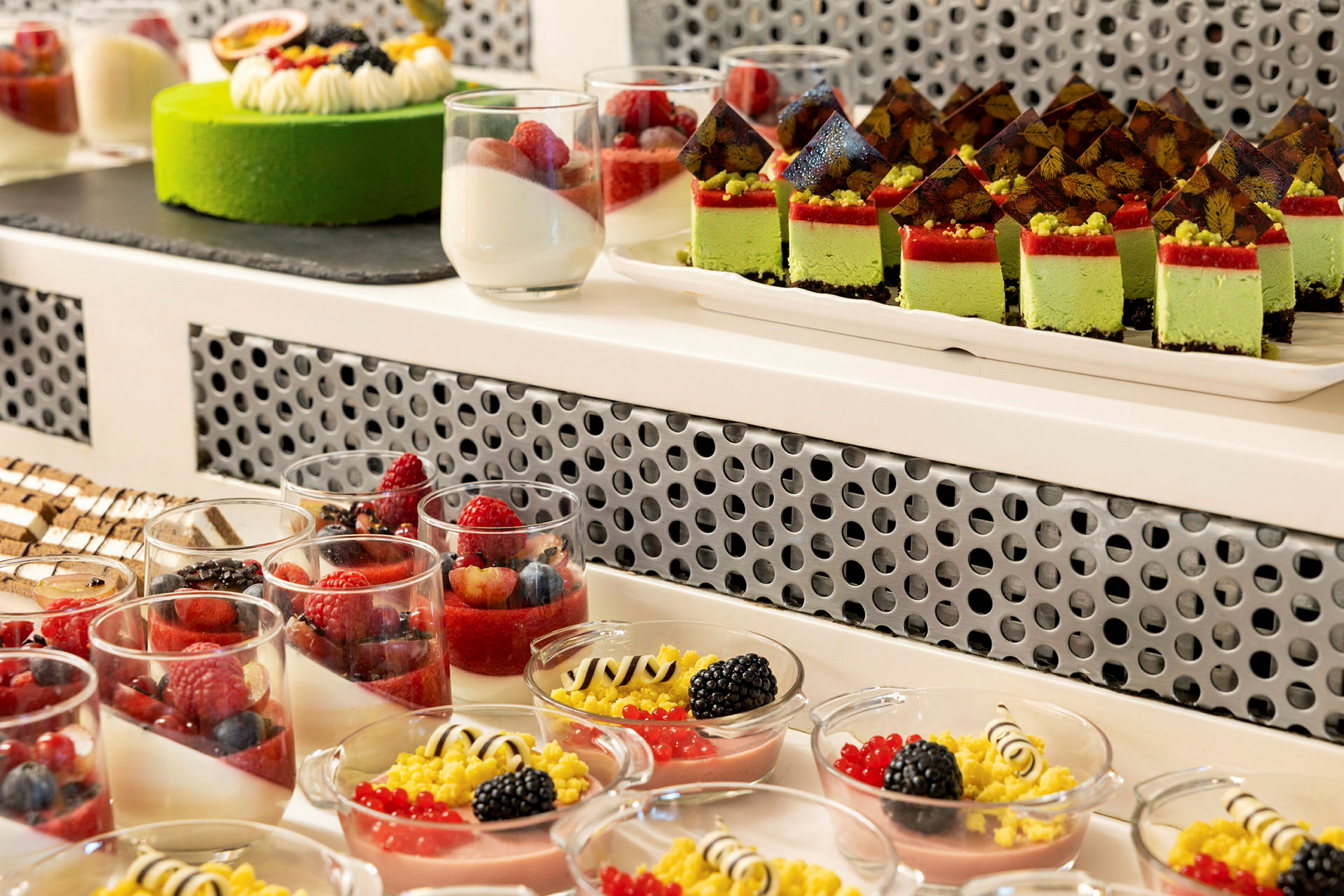 Bilde av ulike fargerike desserter, inkludert glass med frukt, små kakestykker og en grønn kake. (AI-generert tekst)