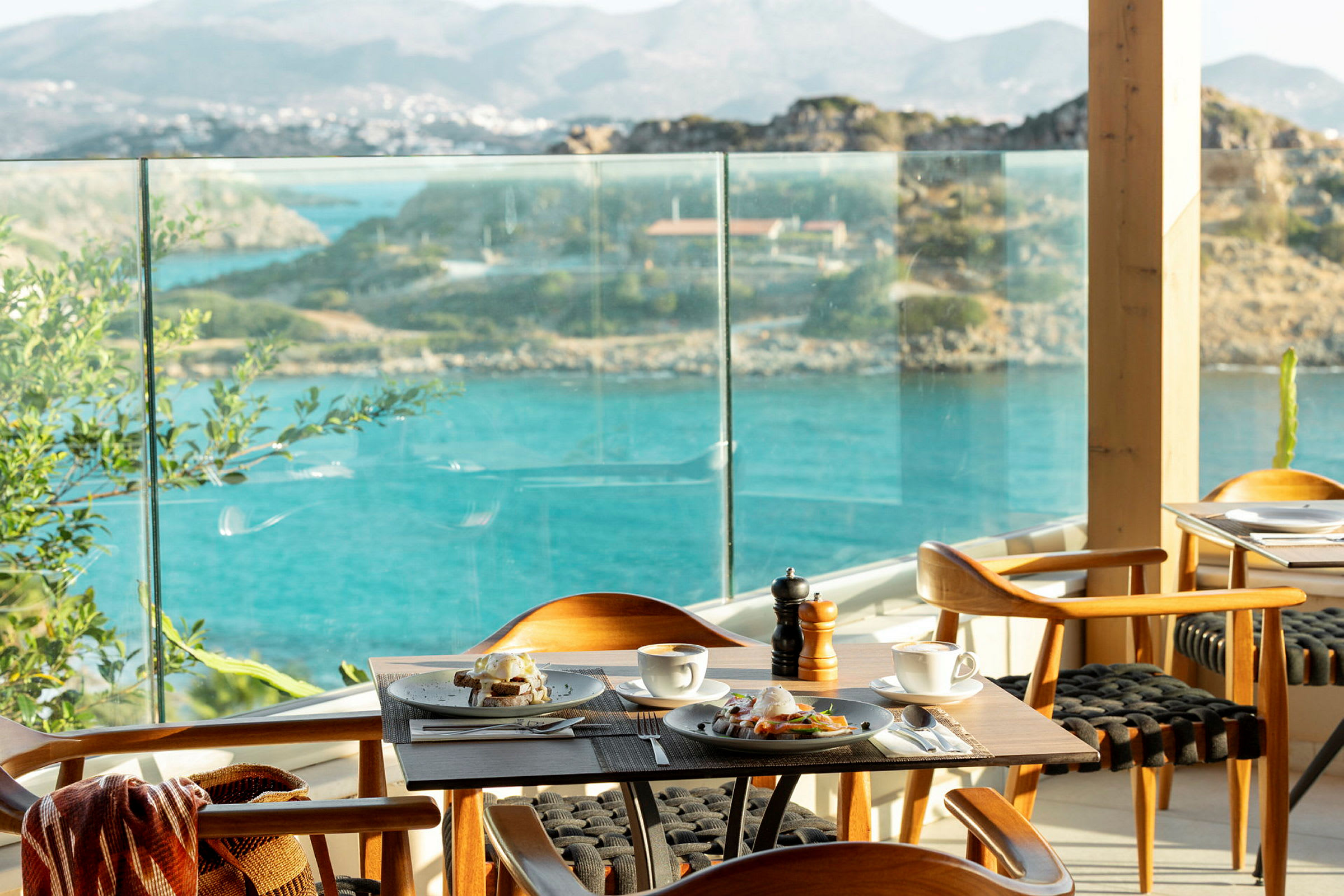 En restaurant med et bord dekket til frokost, med utsikt over havet og det omkringliggende landskapet. (AI-generert tekst)