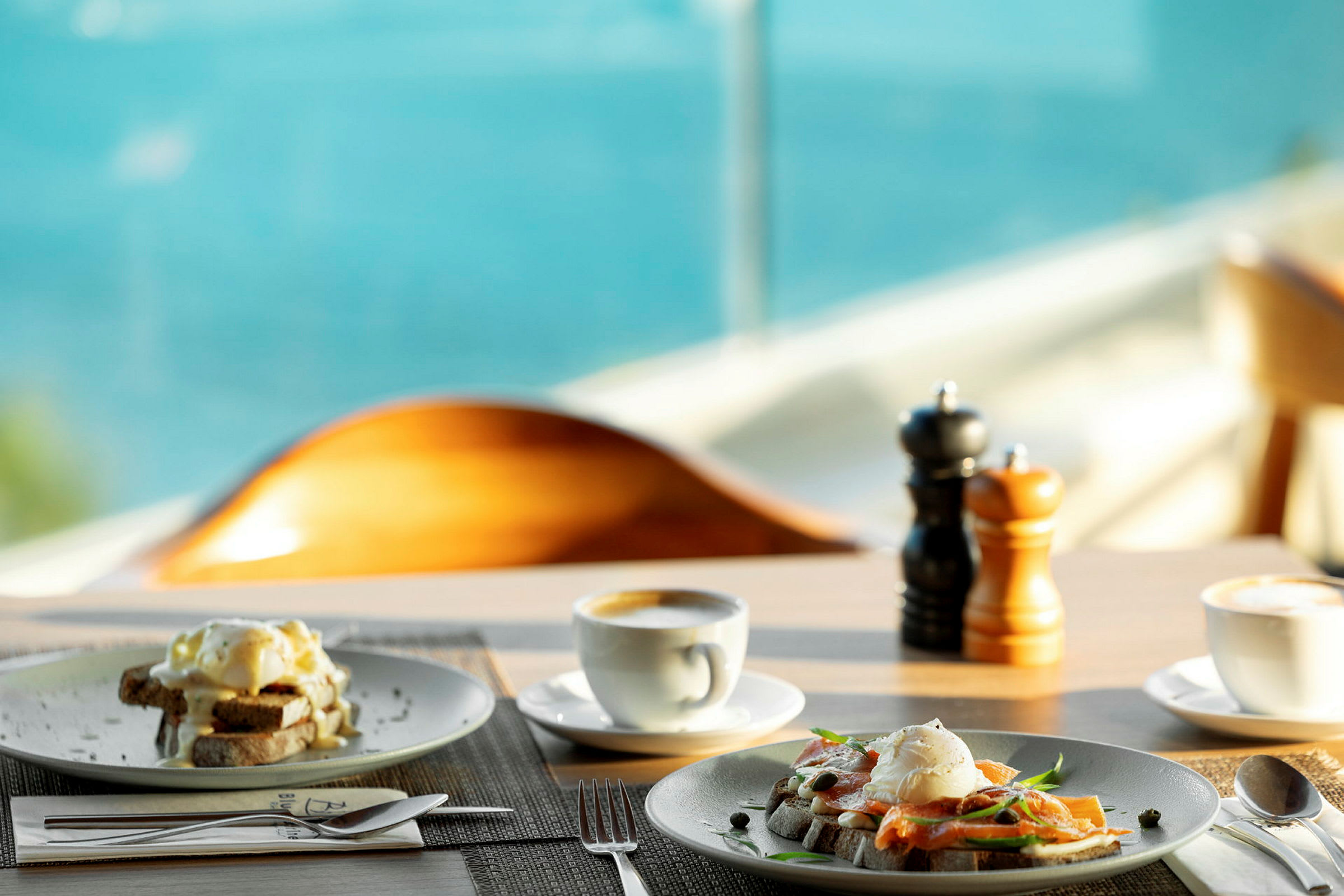 Frokostservering med tallerkener fylt med eggeretter, kaffe og sjøutsikt i bakgrunnen. (AI-generert tekst)