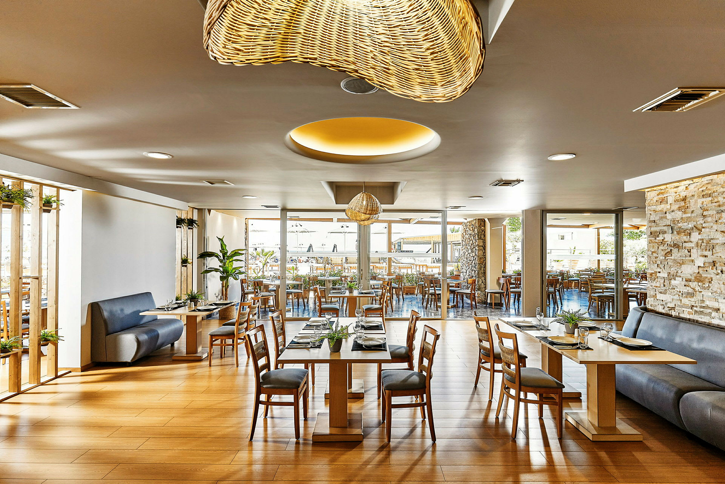 En moderne restaurant med trebord og stoler, dekorativ belysning og store vinduer mot en uteservering. (AI-generert tekst)