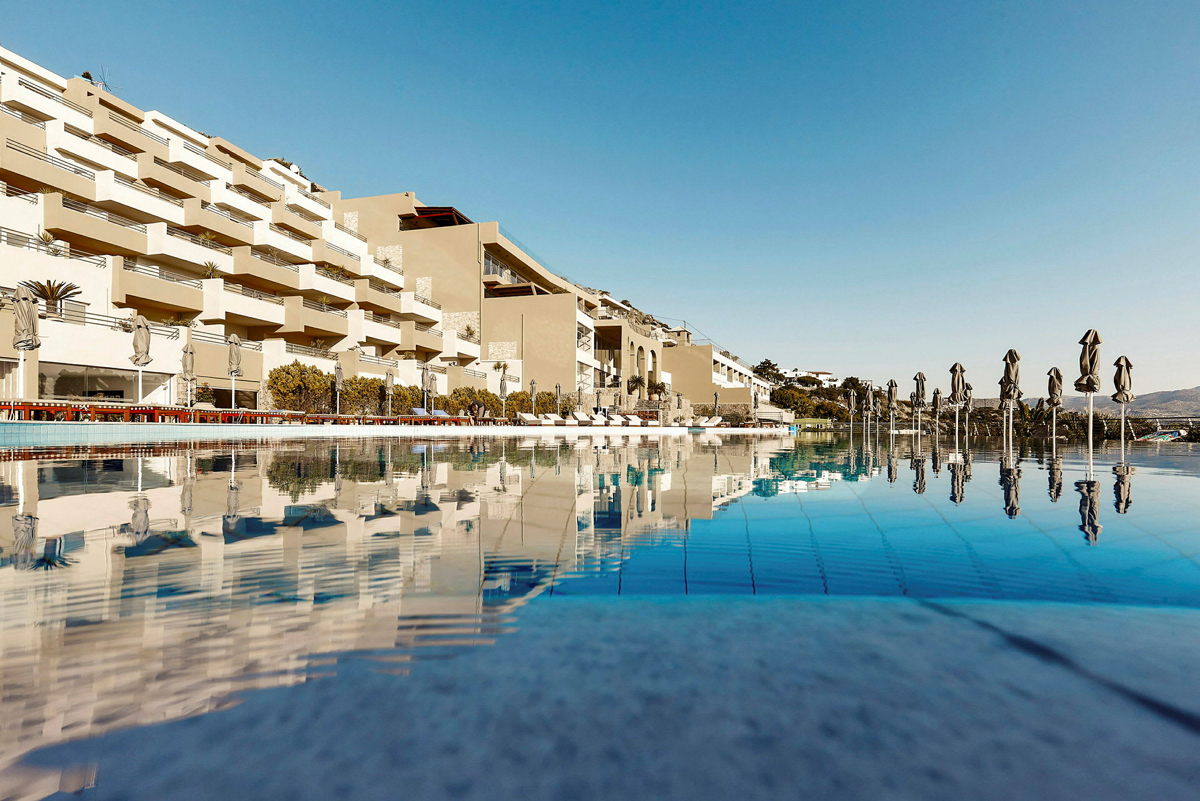 Bilde av en moderne hotellbygning med basseng og solsenger. (AI-generert tekst)