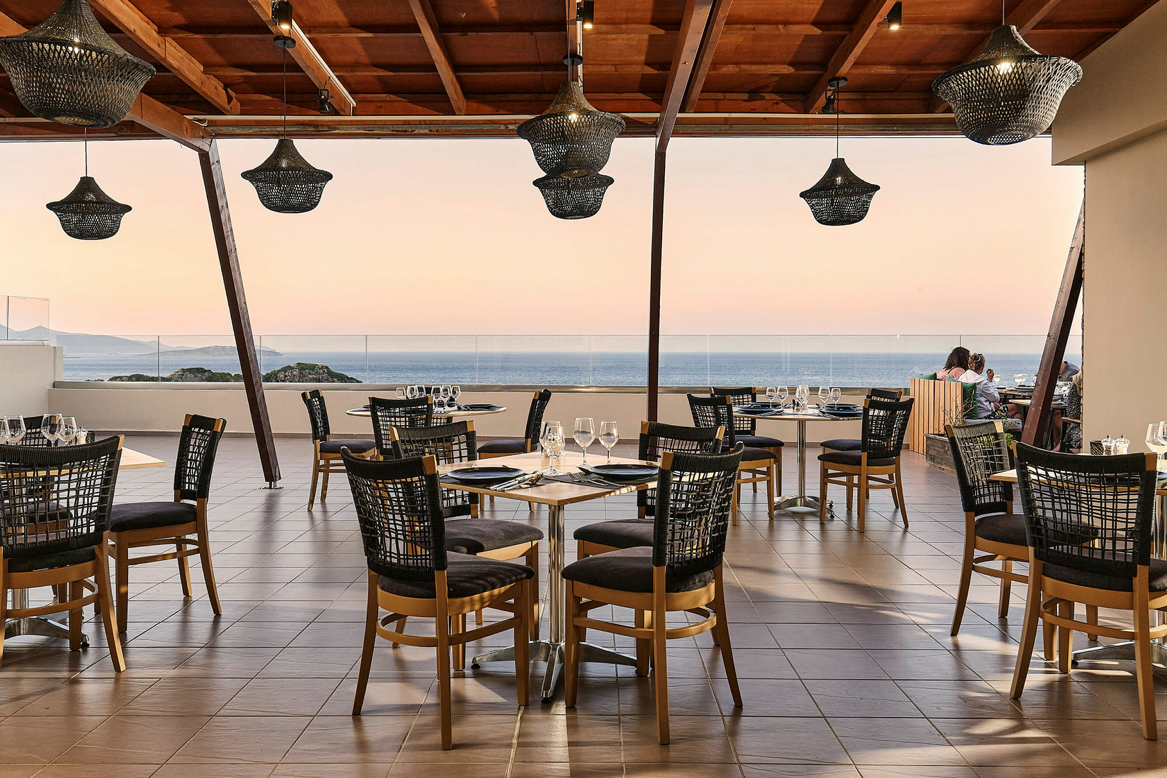 En restaurant med bord og stoler på en terrasse med utsikt over havet. (AI-generert tekst)