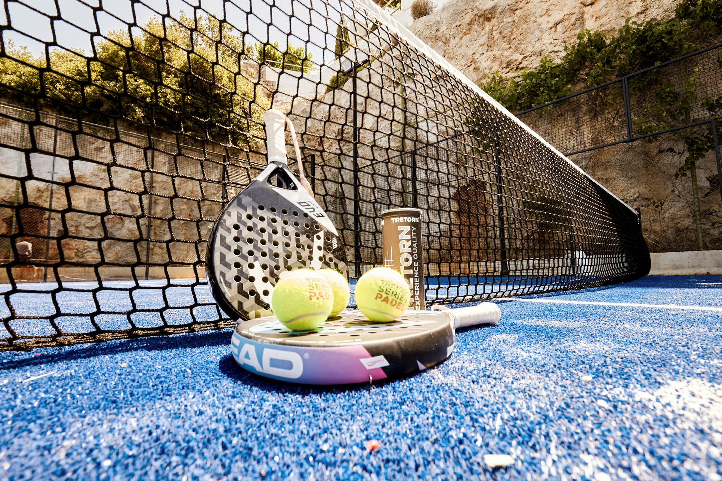 En padelbane med en racket og baller som ligger på den blå matten nær nettet. (AI-generert tekst)
