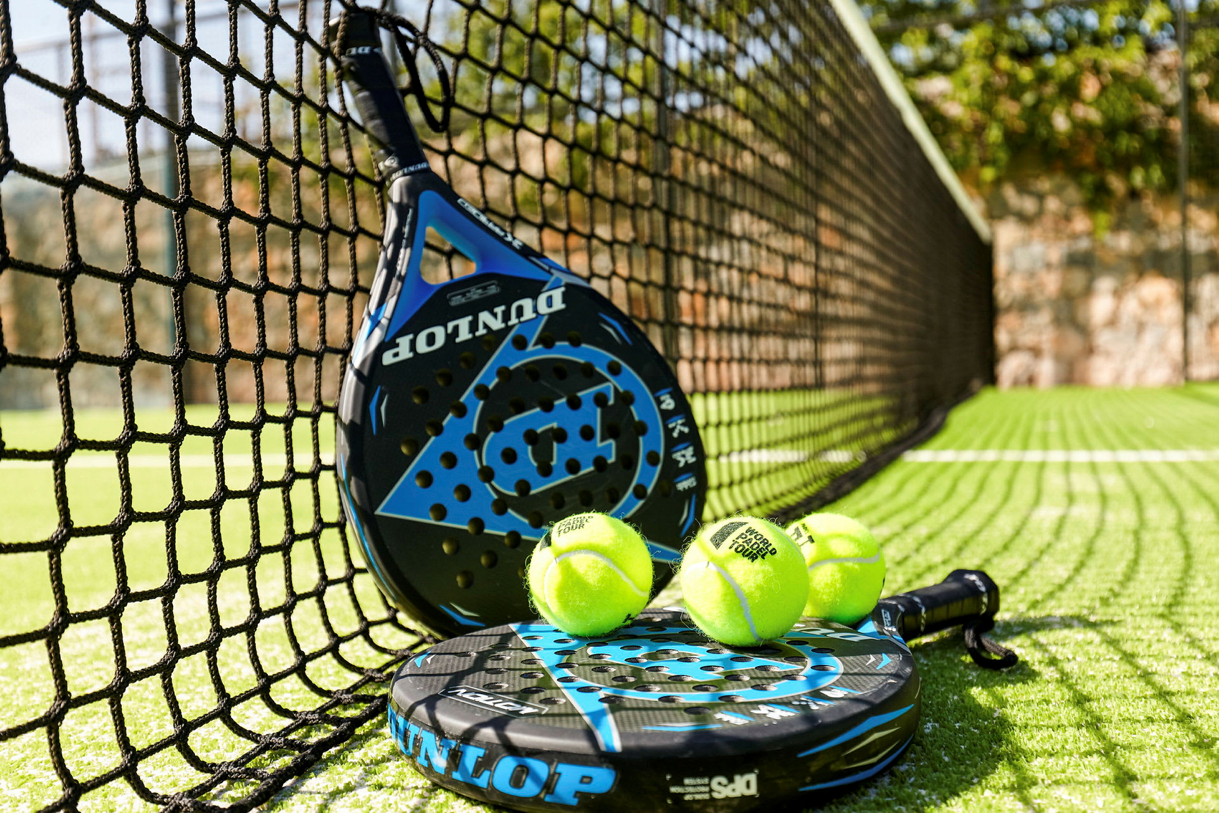 Et padelracket og padelballer ved nettet på en padelbane. (AI-generert tekst)