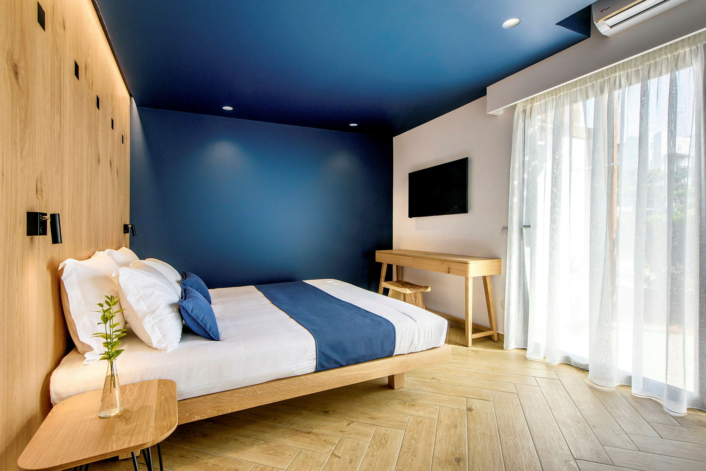 Et moderne hotellrom med blå vegger, en seng med blå sengetepper og treinteriør. (AI-generert tekst)