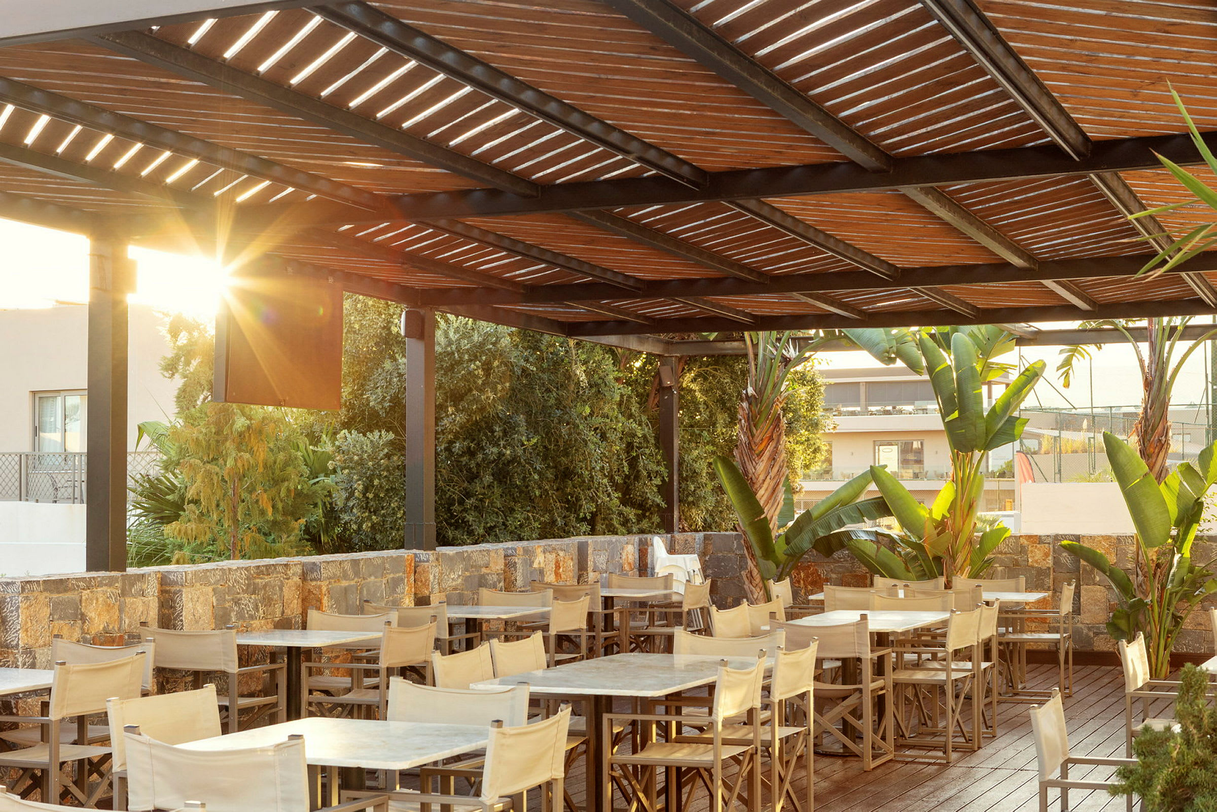 En uterestaurant med bord, stoler, en trepergola og omkringliggende vegetasjon. (AI-generert tekst)