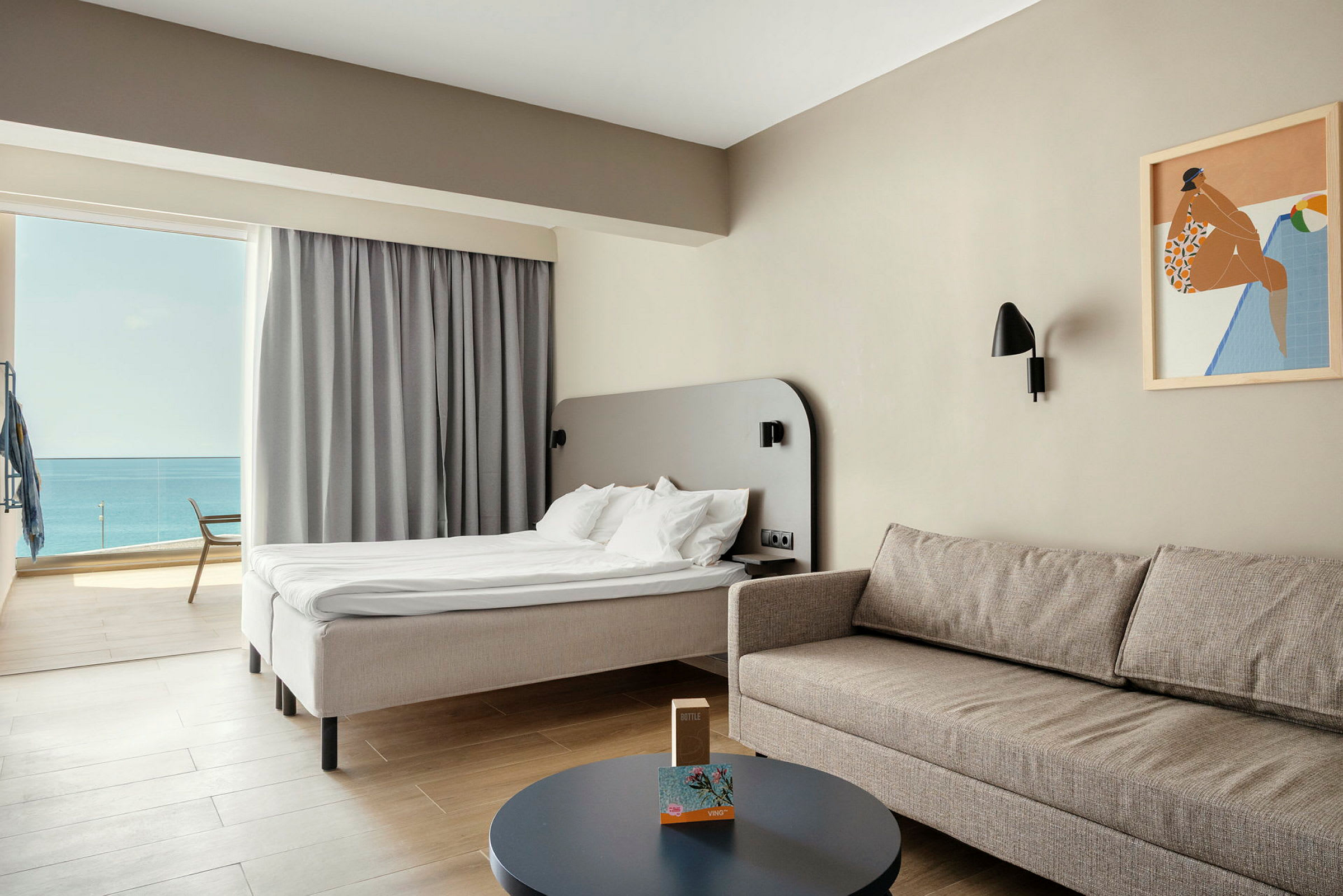 Et deluxe hotellrom med lys innredning, en komfortabel sofa, bord og en seng med utsikt over havet. (AI-generert tekst)