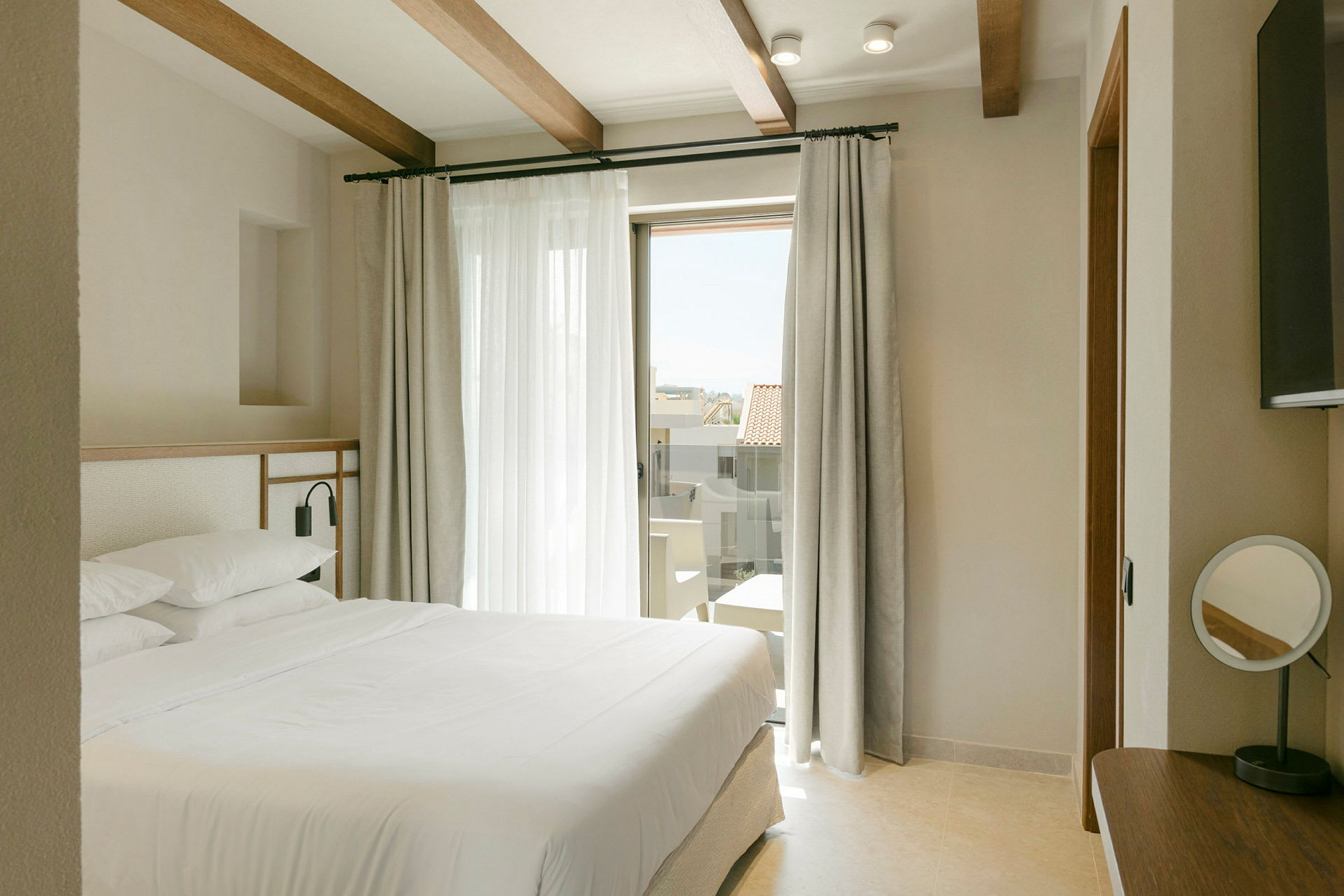 Et moderne hotellrom med en stor seng, lyse gardiner og en glassdør som fører til en balkong. (AI-generert tekst)